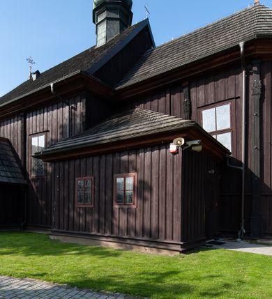 Zdjęcie nr 10: Kościół orientowany, jednonawowy, z węższym, zamkniętym wielobocznie prezbiterium, przy którym od północy prostokątna zakrystia (obecnie skarbiec) od południa prostokątna nowa zakrystia. Przy korpusie od południa i zachodu kruchty. Wewnątrz stropy, w prezbiterium i środkowej części nawy z fasetami; w nawie boczne płaskie odcinki stropu wparte na dwóch słupach. W prezbiterium i nawie na stropach dekoracja geometryczna z listew. Ściany artykułowane pilastrami. Tęcza o wystroju prostokątnym, ujęta przyściennymi filarami. Zewnątrz ściany szalowane deskowaniem na nakładkę, opięte pilastrami. Fasada rozczłonkowana czterema pilastrami wspierającymi gzyms, pośrodku wyłamany nad oknem wchodzącym w pole szczytu. Szczyt trójkątny, w połowie przedzielony gzymsem. Dachy dwuspadowe, nad prezbiterium wielopołaciowy, nad nową zakrystią namiotowy oraz pulpitowe; na kalenicy dachu nawy sygnaturka. Okna prostokątne w profilowanych obramieniach. Portal uszaty, z datą: 1748.