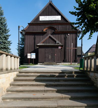 Zdjęcie nr 4: Kościół orientowany, jednonawowy, z węższym, zamkniętym wielobocznie prezbiterium, przy którym od północy prostokątna zakrystia (obecnie skarbiec) od południa prostokątna nowa zakrystia. Przy korpusie od południa i zachodu kruchty. Wewnątrz stropy, w prezbiterium i środkowej części nawy z fasetami; w nawie boczne płaskie odcinki stropu wparte na dwóch słupach. W prezbiterium i nawie na stropach dekoracja geometryczna z listew. Ściany artykułowane pilastrami. Tęcza o wystroju prostokątnym, ujęta przyściennymi filarami. Zewnątrz ściany szalowane deskowaniem na nakładkę, opięte pilastrami. Fasada rozczłonkowana czterema pilastrami wspierającymi gzyms, pośrodku wyłamany nad oknem wchodzącym w pole szczytu. Szczyt trójkątny, w połowie przedzielony gzymsem. Dachy dwuspadowe, nad prezbiterium wielopołaciowy, nad nową zakrystią namiotowy oraz pulpitowe; na kalenicy dachu nawy sygnaturka. Okna prostokątne w profilowanych obramieniach. Portal uszaty, z datą: 1748.