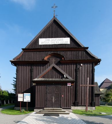 Zdjęcie nr 5: Kościół orientowany, jednonawowy, z węższym, zamkniętym wielobocznie prezbiterium, przy którym od północy prostokątna zakrystia (obecnie skarbiec) od południa prostokątna nowa zakrystia. Przy korpusie od południa i zachodu kruchty. Wewnątrz stropy, w prezbiterium i środkowej części nawy z fasetami; w nawie boczne płaskie odcinki stropu wparte na dwóch słupach. W prezbiterium i nawie na stropach dekoracja geometryczna z listew. Ściany artykułowane pilastrami. Tęcza o wystroju prostokątnym, ujęta przyściennymi filarami. Zewnątrz ściany szalowane deskowaniem na nakładkę, opięte pilastrami. Fasada rozczłonkowana czterema pilastrami wspierającymi gzyms, pośrodku wyłamany nad oknem wchodzącym w pole szczytu. Szczyt trójkątny, w połowie przedzielony gzymsem. Dachy dwuspadowe, nad prezbiterium wielopołaciowy, nad nową zakrystią namiotowy oraz pulpitowe; na kalenicy dachu nawy sygnaturka. Okna prostokątne w profilowanych obramieniach. Portal uszaty, z datą: 1748.