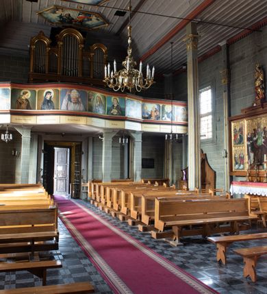 Zdjęcie nr 25: Kościół orientowany, jednonawowy, z węższym, zamkniętym wielobocznie prezbiterium, przy którym od północy prostokątna zakrystia (obecnie skarbiec) od południa prostokątna nowa zakrystia. Przy korpusie od południa i zachodu kruchty. Wewnątrz stropy, w prezbiterium i środkowej części nawy z fasetami; w nawie boczne płaskie odcinki stropu wparte na dwóch słupach. W prezbiterium i nawie na stropach dekoracja geometryczna z listew. Ściany artykułowane pilastrami. Tęcza o wystroju prostokątnym, ujęta przyściennymi filarami. Zewnątrz ściany szalowane deskowaniem na nakładkę, opięte pilastrami. Fasada rozczłonkowana czterema pilastrami wspierającymi gzyms, pośrodku wyłamany nad oknem wchodzącym w pole szczytu. Szczyt trójkątny, w połowie przedzielony gzymsem. Dachy dwuspadowe, nad prezbiterium wielopołaciowy, nad nową zakrystią namiotowy oraz pulpitowe; na kalenicy dachu nawy sygnaturka. Okna prostokątne w profilowanych obramieniach. Portal uszaty, z datą: 1748.