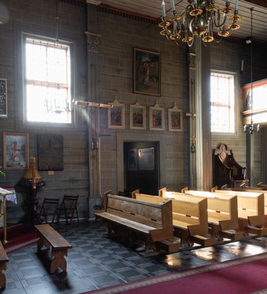 Zdjęcie nr 26: Kościół orientowany, jednonawowy, z węższym, zamkniętym wielobocznie prezbiterium, przy którym od północy prostokątna zakrystia (obecnie skarbiec) od południa prostokątna nowa zakrystia. Przy korpusie od południa i zachodu kruchty. Wewnątrz stropy, w prezbiterium i środkowej części nawy z fasetami; w nawie boczne płaskie odcinki stropu wparte na dwóch słupach. W prezbiterium i nawie na stropach dekoracja geometryczna z listew. Ściany artykułowane pilastrami. Tęcza o wystroju prostokątnym, ujęta przyściennymi filarami. Zewnątrz ściany szalowane deskowaniem na nakładkę, opięte pilastrami. Fasada rozczłonkowana czterema pilastrami wspierającymi gzyms, pośrodku wyłamany nad oknem wchodzącym w pole szczytu. Szczyt trójkątny, w połowie przedzielony gzymsem. Dachy dwuspadowe, nad prezbiterium wielopołaciowy, nad nową zakrystią namiotowy oraz pulpitowe; na kalenicy dachu nawy sygnaturka. Okna prostokątne w profilowanych obramieniach. Portal uszaty, z datą: 1748.