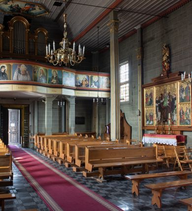 Zdjęcie nr 24: Kościół orientowany, jednonawowy, z węższym, zamkniętym wielobocznie prezbiterium, przy którym od północy prostokątna zakrystia (obecnie skarbiec) od południa prostokątna nowa zakrystia. Przy korpusie od południa i zachodu kruchty. Wewnątrz stropy, w prezbiterium i środkowej części nawy z fasetami; w nawie boczne płaskie odcinki stropu wparte na dwóch słupach. W prezbiterium i nawie na stropach dekoracja geometryczna z listew. Ściany artykułowane pilastrami. Tęcza o wystroju prostokątnym, ujęta przyściennymi filarami. Zewnątrz ściany szalowane deskowaniem na nakładkę, opięte pilastrami. Fasada rozczłonkowana czterema pilastrami wspierającymi gzyms, pośrodku wyłamany nad oknem wchodzącym w pole szczytu. Szczyt trójkątny, w połowie przedzielony gzymsem. Dachy dwuspadowe, nad prezbiterium wielopołaciowy, nad nową zakrystią namiotowy oraz pulpitowe; na kalenicy dachu nawy sygnaturka. Okna prostokątne w profilowanych obramieniach. Portal uszaty, z datą: 1748.