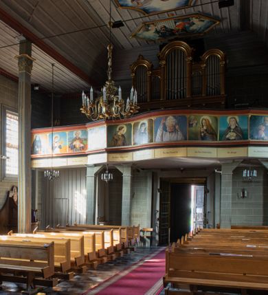 Zdjęcie nr 27: Kościół orientowany, jednonawowy, z węższym, zamkniętym wielobocznie prezbiterium, przy którym od północy prostokątna zakrystia (obecnie skarbiec) od południa prostokątna nowa zakrystia. Przy korpusie od południa i zachodu kruchty. Wewnątrz stropy, w prezbiterium i środkowej części nawy z fasetami; w nawie boczne płaskie odcinki stropu wparte na dwóch słupach. W prezbiterium i nawie na stropach dekoracja geometryczna z listew. Ściany artykułowane pilastrami. Tęcza o wystroju prostokątnym, ujęta przyściennymi filarami. Zewnątrz ściany szalowane deskowaniem na nakładkę, opięte pilastrami. Fasada rozczłonkowana czterema pilastrami wspierającymi gzyms, pośrodku wyłamany nad oknem wchodzącym w pole szczytu. Szczyt trójkątny, w połowie przedzielony gzymsem. Dachy dwuspadowe, nad prezbiterium wielopołaciowy, nad nową zakrystią namiotowy oraz pulpitowe; na kalenicy dachu nawy sygnaturka. Okna prostokątne w profilowanych obramieniach. Portal uszaty, z datą: 1748.