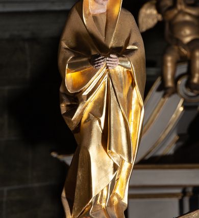 Zdjęcie nr 4: Rzeźby pełnoplastyczne, z tyłu opracowane, umieszczone na belce wygiętej łukiem wklęsło-wypukłym. Chrystus rozpięty na krzyżu w silnym zwisie ciała, z rękami skierowanymi niemal pionowo ku górze, z głową opuszczoną na prawy bark i nogami ugiętymi w kolanach, ze stopami założonymi lewa na prawą, przybitymi do krzyża jednym gwoździem. Biodra osłonięte perizonium ze zwisem tkaniny przy prawym udzie. Na belce krzyża ponad głową Chrystusa titulus z literami: I.N.R.I. Po prawej stronie Chrystusa Maria przedstawiona w całej postaci, zwrócona w trzech czwartych w lewo, w kierunku krzyża; stoi w lekkim kontrapoście, z prawą nogą ugiętą w kolanie, z rękami ugiętymi w łokciach i dłońmi na wysokości piersi. Ubrana w długą suknię z wąskimi rękawami, okryta wraz z głową długim do ziemi płaszczem układającym się sztywnymi, głęboko ciętymi fałdami. Po lewej stronie krzyża św. Jan Ewangelista przedstawiony w całej postaci, frontalnie do widza, stoi w lekkim kontrapoście, z lewą nogą ugiętą w kolanie, rękami ugiętymi w kolanie i dłońmi ułożonymi na wysokości piersi. Młodzieńcza twarz, bez zarostu, z lekko uniesionym podbródkiem i wzrokiem skierowanym ku górze, ujęta długimi, spływającymi na ramiona włosami. Ubrany w długą suknię z szerokimi, pofałdowanymi rękawami oraz zarzucony na ramiona płaszcz z prawą połą przerzuconą przez przód postaci na lewe przedramię i układający się na ziemi u stóp świętego. Karnacje jasne, Chrystusa z ranami, strużkami i kroplami krwi. 