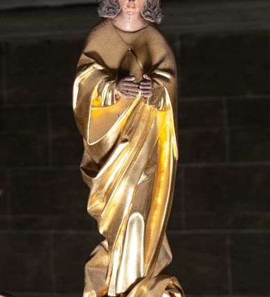 Zdjęcie nr 5: Rzeźby pełnoplastyczne, z tyłu opracowane, umieszczone na belce wygiętej łukiem wklęsło-wypukłym. Chrystus rozpięty na krzyżu w silnym zwisie ciała, z rękami skierowanymi niemal pionowo ku górze, z głową opuszczoną na prawy bark i nogami ugiętymi w kolanach, ze stopami założonymi lewa na prawą, przybitymi do krzyża jednym gwoździem. Biodra osłonięte perizonium ze zwisem tkaniny przy prawym udzie. Na belce krzyża ponad głową Chrystusa titulus z literami: I.N.R.I. Po prawej stronie Chrystusa Maria przedstawiona w całej postaci, zwrócona w trzech czwartych w lewo, w kierunku krzyża; stoi w lekkim kontrapoście, z prawą nogą ugiętą w kolanie, z rękami ugiętymi w łokciach i dłońmi na wysokości piersi. Ubrana w długą suknię z wąskimi rękawami, okryta wraz z głową długim do ziemi płaszczem układającym się sztywnymi, głęboko ciętymi fałdami. Po lewej stronie krzyża św. Jan Ewangelista przedstawiony w całej postaci, frontalnie do widza, stoi w lekkim kontrapoście, z lewą nogą ugiętą w kolanie, rękami ugiętymi w kolanie i dłońmi ułożonymi na wysokości piersi. Młodzieńcza twarz, bez zarostu, z lekko uniesionym podbródkiem i wzrokiem skierowanym ku górze, ujęta długimi, spływającymi na ramiona włosami. Ubrany w długą suknię z szerokimi, pofałdowanymi rękawami oraz zarzucony na ramiona płaszcz z prawą połą przerzuconą przez przód postaci na lewe przedramię i układający się na ziemi u stóp świętego. Karnacje jasne, Chrystusa z ranami, strużkami i kroplami krwi. 