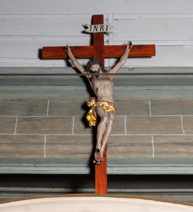 Zdjęcie nr 1: Rzeźby pełnoplastyczne, z tyłu opracowane, umieszczone na belce wygiętej łukiem wklęsło-wypukłym. Chrystus rozpięty na krzyżu w silnym zwisie ciała, z rękami skierowanymi niemal pionowo ku górze, z głową opuszczoną na prawy bark i nogami ugiętymi w kolanach, ze stopami założonymi lewa na prawą, przybitymi do krzyża jednym gwoździem. Biodra osłonięte perizonium ze zwisem tkaniny przy prawym udzie. Na belce krzyża ponad głową Chrystusa titulus z literami: I.N.R.I. Po prawej stronie Chrystusa Maria przedstawiona w całej postaci, zwrócona w trzech czwartych w lewo, w kierunku krzyża; stoi w lekkim kontrapoście, z prawą nogą ugiętą w kolanie, z rękami ugiętymi w łokciach i dłońmi na wysokości piersi. Ubrana w długą suknię z wąskimi rękawami, okryta wraz z głową długim do ziemi płaszczem układającym się sztywnymi, głęboko ciętymi fałdami. Po lewej stronie krzyża św. Jan Ewangelista przedstawiony w całej postaci, frontalnie do widza, stoi w lekkim kontrapoście, z lewą nogą ugiętą w kolanie, rękami ugiętymi w kolanie i dłońmi ułożonymi na wysokości piersi. Młodzieńcza twarz, bez zarostu, z lekko uniesionym podbródkiem i wzrokiem skierowanym ku górze, ujęta długimi, spływającymi na ramiona włosami. Ubrany w długą suknię z szerokimi, pofałdowanymi rękawami oraz zarzucony na ramiona płaszcz z prawą połą przerzuconą przez przód postaci na lewe przedramię i układający się na ziemi u stóp świętego. Karnacje jasne, Chrystusa z ranami, strużkami i kroplami krwi. 