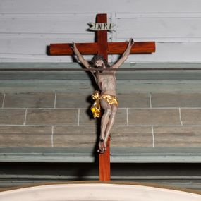 Zdjęcie nr 1: Rzeźby pełnoplastyczne, z tyłu opracowane, umieszczone na belce wygiętej łukiem wklęsło-wypukłym. Chrystus rozpięty na krzyżu w silnym zwisie ciała, z rękami skierowanymi niemal pionowo ku górze, z głową opuszczoną na prawy bark i nogami ugiętymi w kolanach, ze stopami założonymi lewa na prawą, przybitymi do krzyża jednym gwoździem. Biodra osłonięte perizonium ze zwisem tkaniny przy prawym udzie. Na belce krzyża ponad głową Chrystusa titulus z literami: I.N.R.I. Po prawej stronie Chrystusa Maria przedstawiona w całej postaci, zwrócona w trzech czwartych w lewo, w kierunku krzyża; stoi w lekkim kontrapoście, z prawą nogą ugiętą w kolanie, z rękami ugiętymi w łokciach i dłońmi na wysokości piersi. Ubrana w długą suknię z wąskimi rękawami, okryta wraz z głową długim do ziemi płaszczem układającym się sztywnymi, głęboko ciętymi fałdami. Po lewej stronie krzyża św. Jan Ewangelista przedstawiony w całej postaci, frontalnie do widza, stoi w lekkim kontrapoście, z lewą nogą ugiętą w kolanie, rękami ugiętymi w kolanie i dłońmi ułożonymi na wysokości piersi. Młodzieńcza twarz, bez zarostu, z lekko uniesionym podbródkiem i wzrokiem skierowanym ku górze, ujęta długimi, spływającymi na ramiona włosami. Ubrany w długą suknię z szerokimi, pofałdowanymi rękawami oraz zarzucony na ramiona płaszcz z prawą połą przerzuconą przez przód postaci na lewe przedramię i układający się na ziemi u stóp świętego. Karnacje jasne, Chrystusa z ranami, strużkami i kroplami krwi. 