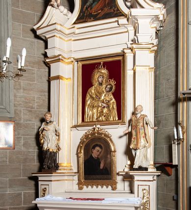 Zdjęcie nr 2: Ołtarz jednoosiowy, jednokondygnacyjny, ze zwieńczeniem. Mensa umieszczona na tumbie zwężającej się ku dołowi, ozdobionej od czoła płyciną prostokątną w złoconym obramieniu, pośrodku ze splecionymi literami imienia Maria. Nastawa flankowana ustawionymi ukośnie czworobocznymi, kanelowanymi filarami, dźwigającymi odcinki pełnego belkowania i gzymsu, przerwanych nad polem środkowym. Na tle filarów umieszczone na konsolach rzeźby: św. Stanisława Kostki (po lewej) i św. Ignacego Loyoli (po prawej). W polu środkowym, nad mensą zawieszony obraz w ozdobnej ramie z przedstawieniem św. Stanisława Kostki w półpostaci; wyżej prostokątna nisza, w której obraz Matki Boskiej z Dzieciątkiem. Zwieńczenie w kształcie aediculi zamkniętej łukiem półkolistym nadwieszonym, w której polu obraz z przedstawieniem św. Józefa w półpostaci. Po bokach, w osiach filarów odcinki przerwanego przyczółka na których rzeźby nagich, uskrzydlonych puttów.  Na gzymsie wieńczącym ołtarz Gołębica Ducha Świętego wśród promieni.