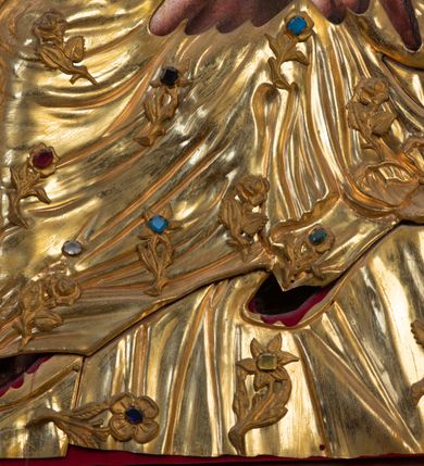 Zdjęcie nr 13: Przedstawienie Matki Boskiej z Dzieciątkiem w typie Matki Boskiej Śnieżnej. Twarz Marii, głowa i stopy Dzieciątka oraz dłonie malowane; szaty Marii i Dzieciątka promieniste nimby wokół głów oraz zamknięte korony wykonane z trybowanej złoconej blachy, ozdobione motywami kwiatów i kameryzacją. Tło z czerwonego aksamitu.