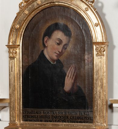 Zdjęcie nr 7: Obraz w kształcie prostokąta zamkniętego półkoliście z przedstawieniem św. Stanisława Kostki. Święty ukazany w półpostaci, zwrócony w trzech czwartych w lewo, z pochyloną głową, rękami zgiętymi w łokciach i dłońmi złożonymi do modlitwy na wysokości piersi. Twarz młodzieńcza, o jasnej karnacji. Ubrany w czarną sutannę jezuicką. Tło monochromatyczne, rozświetlone za głową świętego. U dołu obrazu napis czarną kapitałą na jasnym tle: S STANISLAUS KOSTKA SOCIETATIS IESU / PATRONUS HUIUS PAROCHIE QUAM(QUE) PESTE / HOMINUM ANNO 1678 LIBERAVIT. Obraz w drewnianej złoconej ramie w kształcie półkolistej arkady z kanelowanymi pilastrami, nadwieszonymi na konsolkach, z ażurowym fryzem arkadkowym u dołu. 