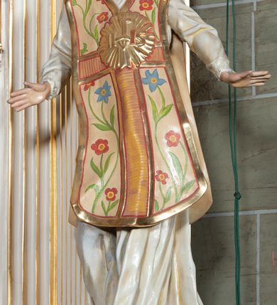 Zdjęcie nr 5: Rzeźba pełnoplastyczna, przyścienna; całopostaciowe przedstawienie św. Ignacego Loyoli, ukazanego frontalnie, stojącego w dynamicznej pozie, z esowato wygiętym ciałem, z prawą stopą wysuniętą do przodu, z rękami odwiedzionymi od ciała na boki, z głową przechyloną na lewy bark. Głowa starszego mężczyzny, z łysą czaszką, okolona wianuszkiem siwych włosów; twarz pociągła o jasnej karnacji, z zaróżowionymi policzkami, długim nosem i oczami skierowanymi ku górze, okolona obfitym siwym zarostem. Święty ubrany w długą albę ozdobioną u dołu koronką oraz ornat ozdobiony złotym galonem, bokami z motywem wici z barwnych kwiatów na białym tle i pretekstą w kształcie litery tau. Na piersiach okazały płaskorzeźbiony, kolisty złoty medalion z literami IHS w glorii promienistej. 