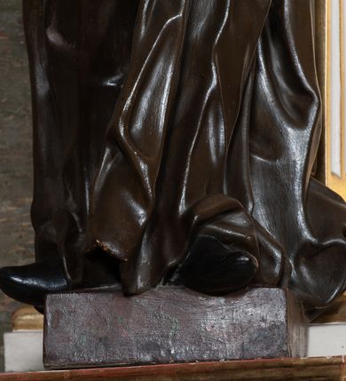 Zdjęcie nr 5: Rzeźba pełnoplastyczna, przyścienna; całopostaciowe przedstawienie św. Stanisława Kostki, ukazanego frontalnie, stojącego w ożywionej pozie, z esowato wygiętym ciałem, z prawą stopą wysuniętą do przodu, z lewą ręką wysuniętą do przodu i prawą dłonią złożoną na piersi, z głową lekko przechyloną na lewy bark., w; Twarz młodego mężczyzny o niemal jeszcze dziecięcych rysach, o jasnej karnacji, z zaróżowionymi policzkami, długim nosem i oczami skierowanymi w dół. Święty ubrany w udrapowane dynamicznie czarną sutannę jezuicką i białą komżę ozdobioną złotą koronką.