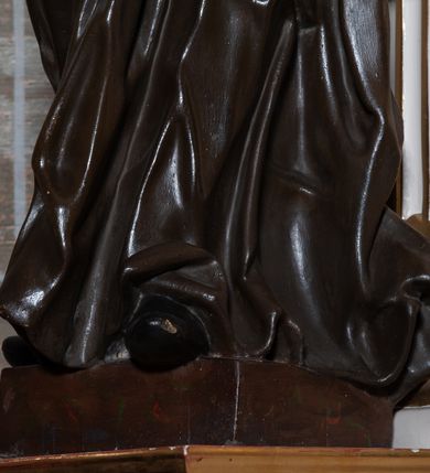 Zdjęcie nr 6: Rzeźba pełnoplastyczna, przyścienna; całopostaciowe przedstawienie św. Stanisława Kostki, ukazanego frontalnie, stojącego w ożywionej pozie, z esowato wygiętym ciałem, z prawą stopą wysuniętą do przodu, z lewą ręką wysuniętą do przodu i prawą dłonią złożoną na piersi, z głową lekko przechyloną na lewy bark., w; Twarz młodego mężczyzny o niemal jeszcze dziecięcych rysach, o jasnej karnacji, z zaróżowionymi policzkami, długim nosem i oczami skierowanymi w dół. Święty ubrany w udrapowane dynamicznie czarną sutannę jezuicką i białą komżę ozdobioną złotą koronką.