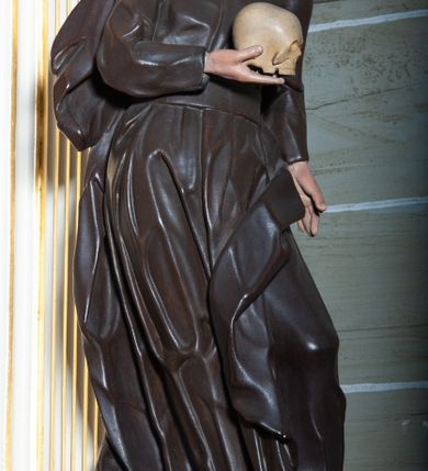 Zdjęcie nr 3: Rzeźba pełnoplastyczna, przyścienna ukazująca jezuickiego świętego św. Franciszka Borgiasza w całej postaci, w ujęciu frontalnym. Święty o szczupłej sylwetce stoi w kontrapoście, z lewą nogą ugiętą w kolanie i wysuniętą stopą, z głową przechyloną na prawy bark. Lewa ręka opuszczona wzdłuż tułowia, w prawej ugiętej w łokciu trzyma na wysokości piersi czaszkę ludzką. Twarz szczupła, o jasnej karnacji, z długim nosem i wzrokiem skierowanym d dół; włosy krótkie, zmierzwione. Ubrany w czarną sutannę jezuicką i płaszcz. 