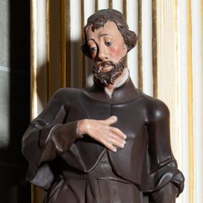 Zdjęcie nr 1: Rzeźba pełnoplastyczna, przyścienna, ukazująca jezuickiego świętego św. Franciszka Ksawerego w całej postaci, w ujęciu frontalnym. Święty o szczupłej sylwetce stoi w kontrapoście, z lewą nogą ugiętą w kolanie i wysuniętą lewą stopą, z głową przechyloną na prawy bark. Lewa ręka ugięta w łokciu z dłonią wysuniętą do przodu; prawa dłoń złożona na piersi. Twarz pociągła, z długim nosem, wydatnymi kośćmi policzkowymi i wzrokiem skierowanym d dół, okolona krótkimi włosami i krótkim ciemnym zarostem. Karnacja jasna z zaróżowionymi policzkami. Ubrany w czarną sutannę jezuicką z czarną pelerynką.