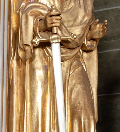 Zdjęcie nr 3: Rzeźba pełnoplastyczna, przyścienna, ustawiona na prostopadłościennym, wykonanym z czarnego marmuru relikwiarzu różnych świętych. Święty przedstawiony w całej postaci, stoi w lekkim kontrapoście, z rękami ugiętymi w łokciach, prawą dłonią trzyma rękojeść długiego srebrzystego miecza. Twarz pociągła okolona kędzierzawymi siwymi włosami i długą brodą. Ubrany w długą, sięgającą do kostek złotą  suknię i zarzucony na ramiona złoty płaszcz. 