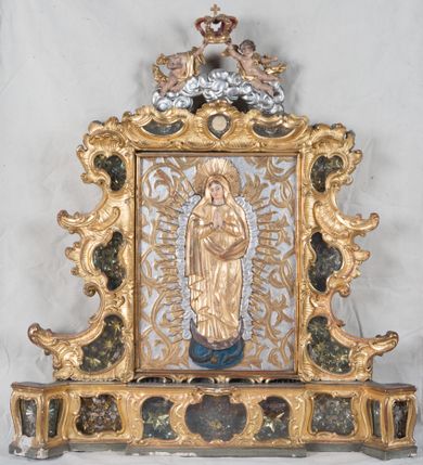 Zdjęcie nr 1: Feretron dwustronny z płaskorzeźbą Najświętszej Marii Panny Niepokalanie Poczętej na awersie oraz płaskorzeźbą ze sceną Narodzenia Najświętszej Marii Panny na rewersie, ustawiony na niskim postumencie o fantazyjnym wykroju z osią główną wysuniętą do przodu oraz narożnikami ustawionymi ukośnie. W postumencie dziewięć przeszklonych gablotek mieszczących relikwie świętych, które opisane są na małych karteczkach, otoczone różnego rodzaju kwiatkami  i gwiazdkami wykonanymi z papieru i cienkich blaszek. Otwory gablotek  o różnorodnym, fantazyjnym, opływowym wykroju. Na górnej powierzchni podstawy, po bokach małe otwory po zatkniętych w nich, niezachowanych rzeźbach apostołów. Rama obrazów w kształcie stojącego prostokąta, ujęta po każdej stronie trzema gablotkami otoczonymi rzeźbionym ornamentem rocaille&#039;owym. W zwieńczeniu takie same, mniejsze gablotki, pośrodku zamiast relikwii owalna plakietka z kości z przedstawieniem Ucieczki do Egiptu. W zwieńczeniu na obłokach dwa aniołki podtrzymujące koronę. Na rewersie struktura feretronu o takim samym kształcie. Podstawa zdobiona gęstą wicią ze stylizowanych liści akantu zamkniętą w kształcie prostokąta leżącego.  Po bokach zamiast gablotek owoidalne pola, w których znajduje się złocona, drobna kratka.  W zwieńczeniu, w polu środkowym monogram Marii, powyżej aniołki trzymające koronę widoczne od tyłu.

Na awersie płaskorzeźba z przedstawieniem Najświętszej Marii Panny Niepokalanie Poczętej. Maria ukazana w postawie stojącej, frontalnie, na półksiężycu  i globie ziemskim, depcząca bosymi stopami węża, ze złożonymi w geście modlitwy rękami, z głową delikatnie przechyloną w prawą stronę. Twarz owalna z małymi i wąskimi ustami, wzrokiem skierowanym w dal. Włosy jasnobrązowe z przedziałkiem pośrodku, skryte pod płaszczem. Ubrana w długą, złoconą suknię z długimi rękawami, przewiązaną pod biustem oraz złoty płaszcz założony  na głowę i otulający całą postać, z lewym końcem przerzuconym przez prawe przedramię. W dolnej partii płaszcza oraz na prawej piersi ryta dekoracja roślinna, składająca się z sześciu ulistnionych gałązek z pięcio- lub sześciopłatkowymi kwiatkami. Wokół całej postaci Marii otok z srebrnych obłoków oraz promieni naprzemiennie prostych  i falujących. Wokół głowy złoty, kolisty nimb z gęsto ułożonych promieni; na nim okrąg z gwiazd dwunastu, częściowo nie zachowany. Tło srebrne, zdobione złoconą  i płaskorzeźbioną wicią z liści stylizujących suchy akant.

Na rewersie płaskorzeźba z przedstawieniem Narodzenia Najświętszej Marii Panny. Kompozycja dwustrefowa, w dolnej partii ukazani św. Joachim i św. Anna, w górnej Bóg Ojciec i Matka Boska w otoczeniu uskrzydlonych główek anielskich. Rodzice Marii w pozycji klęczącej, zwróceni trzy czwarte  ku środkowi. Ubrani w długie i złocone suknie z długimi rękawami oraz złote płaszcze, św. Anna z welonem na głowie. Pomiędzy nimi ustawiona ukośnie kołyska, ozdobiona na narożu uskrzydloną główką aniołka, przykryta długą tkaniną. U nóg św. Anny zamknięta księga, na obwolucie zdobiona prostym, łacińskim krzyżykiem. Po prawej stronie obrazu, za św. Anną, na wysokim postumencie antykizujący dzban. W górnej partii kompozycji Bóg Ojciec widoczny w półpostaci, frontalnie,  w lewym ręku trzymający jabłko królewskie, prawą wyciągający ku Marii. Ubrany  w złotą szatę z długimi rękawami oraz złoty płaszcz z rozwianym jednym końcem  po jego prawej stronie, wokół głowy złoty i trójkątny nimb. Twarz okolona gęstą i siwą brodą oraz siwymi, średniej długości włosami. Maria ukazana poniżej Boga Ojca,  w młodzieńczym wieku, w postawie stojącej na półksiężycu, frontalnie, z rękami złożonymi w geście modlitwy. Ubrana w długą i złotą suknię z długimi rękawami oraz złoty płaszcz, którego koniec przerzucony przez lewe ramię; wokół głowy złoty okrągły nimb. Włosy długie i jasnobrązowe, opadające na plecy. Tło utworzone  z obłoków. Wokół Boga Ojca i Marii cztery uskrzydlone główki aniołków o wyraźnie zaznaczonych pucułowatych policzkach. 

Relikwie  świętych umieszczone w niewielkich gablotkach za szybkami, opisane na karteczkach. Zwieńczenie feretronu, od lewej: nierozpoznane relikwie świętego, plakietka z kości  z przedstawieniem Ucieczki do Egiptu, relikwie „Sancta THERESIA Virgo”  Prawy bok feretronu, od góry: relikwie „Sanctae Katarzyny Panny”, relikwie „Sanctae Rozalii Panny”, relikwie „Sancta Illuminata Martir”. Podstawa feretronu, od lewej: relikwie „Sanctus Benedicti Martyr, Sancta Victoria Virgo Martyr, Sancti Floryana Męczennika”; relikwie „Sanctae Marciana Virgo Martyr”; relikwie  „Sanctus Quirini Martir”; relikwie „Sancti Jucundina Martyr”; relikwie „Sanctus Mansueti M.,  Sancta Eugenia Virgo Martyr, Sanctae Bronisławy”. Lewy bok feretronu, od góry: relikwie „Sanctus Jana Kantego”, relikwie „Sanctae Honorati Martyr”, relikwie „Sancta Illuminata Martir”. Plakietka ze sceną ucieczki do Egiptu o kształcie owalnym. W centrum kompozycji ukazani św. Józef oraz Maria z Dzieciątkiem Jezus na osiołku. Wokół słabo czytelny napis: „Cetur doms(e) in aeg vivo[?].” Rzeźby aniołków w zwieńczeniu usytuowane przeciwstawnie, diagonalnie, zwrócone górną partią ciała ku środkowi, jedną ręką podtrzymujące koronę. Ubrane w wąską tkaninę przerzuconą przez jedno z ramion i zwiewnie opadającą w dół. Korona w typie zamkniętym. Struktura feretronu złocona i srebrzona.	