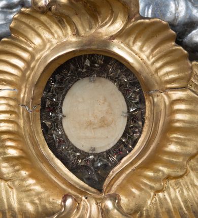 Zdjęcie nr 6: Feretron dwustronny z płaskorzeźbą Najświętszej Marii Panny Niepokalanie Poczętej na awersie oraz płaskorzeźbą ze sceną Narodzenia Najświętszej Marii Panny na rewersie, ustawiony na niskim postumencie o fantazyjnym wykroju z osią główną wysuniętą do przodu oraz narożnikami ustawionymi ukośnie. W postumencie dziewięć przeszklonych gablotek mieszczących relikwie świętych, które opisane są na małych karteczkach, otoczone różnego rodzaju kwiatkami  i gwiazdkami wykonanymi z papieru i cienkich blaszek. Otwory gablotek  o różnorodnym, fantazyjnym, opływowym wykroju. Na górnej powierzchni podstawy, po bokach małe otwory po zatkniętych w nich, niezachowanych rzeźbach apostołów. Rama obrazów w kształcie stojącego prostokąta, ujęta po każdej stronie trzema gablotkami otoczonymi rzeźbionym ornamentem rocaille&#039;owym. W zwieńczeniu takie same, mniejsze gablotki, pośrodku zamiast relikwii owalna plakietka z kości z przedstawieniem Ucieczki do Egiptu. W zwieńczeniu na obłokach dwa aniołki podtrzymujące koronę. Na rewersie struktura feretronu o takim samym kształcie. Podstawa zdobiona gęstą wicią ze stylizowanych liści akantu zamkniętą w kształcie prostokąta leżącego.  Po bokach zamiast gablotek owoidalne pola, w których znajduje się złocona, drobna kratka.  W zwieńczeniu, w polu środkowym monogram Marii, powyżej aniołki trzymające koronę widoczne od tyłu.

Na awersie płaskorzeźba z przedstawieniem Najświętszej Marii Panny Niepokalanie Poczętej. Maria ukazana w postawie stojącej, frontalnie, na półksiężycu  i globie ziemskim, depcząca bosymi stopami węża, ze złożonymi w geście modlitwy rękami, z głową delikatnie przechyloną w prawą stronę. Twarz owalna z małymi i wąskimi ustami, wzrokiem skierowanym w dal. Włosy jasnobrązowe z przedziałkiem pośrodku, skryte pod płaszczem. Ubrana w długą, złoconą suknię z długimi rękawami, przewiązaną pod biustem oraz złoty płaszcz założony  na głowę i otulający całą postać, z lewym końcem przerzuconym przez prawe przedramię. W dolnej partii płaszcza oraz na prawej piersi ryta dekoracja roślinna, składająca się z sześciu ulistnionych gałązek z pięcio- lub sześciopłatkowymi kwiatkami. Wokół całej postaci Marii otok z srebrnych obłoków oraz promieni naprzemiennie prostych  i falujących. Wokół głowy złoty, kolisty nimb z gęsto ułożonych promieni; na nim okrąg z gwiazd dwunastu, częściowo nie zachowany. Tło srebrne, zdobione złoconą  i płaskorzeźbioną wicią z liści stylizujących suchy akant.

Na rewersie płaskorzeźba z przedstawieniem Narodzenia Najświętszej Marii Panny. Kompozycja dwustrefowa, w dolnej partii ukazani św. Joachim i św. Anna, w górnej Bóg Ojciec i Matka Boska w otoczeniu uskrzydlonych główek anielskich. Rodzice Marii w pozycji klęczącej, zwróceni trzy czwarte  ku środkowi. Ubrani w długie i złocone suknie z długimi rękawami oraz złote płaszcze, św. Anna z welonem na głowie. Pomiędzy nimi ustawiona ukośnie kołyska, ozdobiona na narożu uskrzydloną główką aniołka, przykryta długą tkaniną. U nóg św. Anny zamknięta księga, na obwolucie zdobiona prostym, łacińskim krzyżykiem. Po prawej stronie obrazu, za św. Anną, na wysokim postumencie antykizujący dzban. W górnej partii kompozycji Bóg Ojciec widoczny w półpostaci, frontalnie,  w lewym ręku trzymający jabłko królewskie, prawą wyciągający ku Marii. Ubrany  w złotą szatę z długimi rękawami oraz złoty płaszcz z rozwianym jednym końcem  po jego prawej stronie, wokół głowy złoty i trójkątny nimb. Twarz okolona gęstą i siwą brodą oraz siwymi, średniej długości włosami. Maria ukazana poniżej Boga Ojca,  w młodzieńczym wieku, w postawie stojącej na półksiężycu, frontalnie, z rękami złożonymi w geście modlitwy. Ubrana w długą i złotą suknię z długimi rękawami oraz złoty płaszcz, którego koniec przerzucony przez lewe ramię; wokół głowy złoty okrągły nimb. Włosy długie i jasnobrązowe, opadające na plecy. Tło utworzone  z obłoków. Wokół Boga Ojca i Marii cztery uskrzydlone główki aniołków o wyraźnie zaznaczonych pucułowatych policzkach. 

Relikwie  świętych umieszczone w niewielkich gablotkach za szybkami, opisane na karteczkach. Zwieńczenie feretronu, od lewej: nierozpoznane relikwie świętego, plakietka z kości  z przedstawieniem Ucieczki do Egiptu, relikwie „Sancta THERESIA Virgo”  Prawy bok feretronu, od góry: relikwie „Sanctae Katarzyny Panny”, relikwie „Sanctae Rozalii Panny”, relikwie „Sancta Illuminata Martir”. Podstawa feretronu, od lewej: relikwie „Sanctus Benedicti Martyr, Sancta Victoria Virgo Martyr, Sancti Floryana Męczennika”; relikwie „Sanctae Marciana Virgo Martyr”; relikwie  „Sanctus Quirini Martir”; relikwie „Sancti Jucundina Martyr”; relikwie „Sanctus Mansueti M.,  Sancta Eugenia Virgo Martyr, Sanctae Bronisławy”. Lewy bok feretronu, od góry: relikwie „Sanctus Jana Kantego”, relikwie „Sanctae Honorati Martyr”, relikwie „Sancta Illuminata Martir”. Plakietka ze sceną ucieczki do Egiptu o kształcie owalnym. W centrum kompozycji ukazani św. Józef oraz Maria z Dzieciątkiem Jezus na osiołku. Wokół słabo czytelny napis: „Cetur doms(e) in aeg vivo[?].” Rzeźby aniołków w zwieńczeniu usytuowane przeciwstawnie, diagonalnie, zwrócone górną partią ciała ku środkowi, jedną ręką podtrzymujące koronę. Ubrane w wąską tkaninę przerzuconą przez jedno z ramion i zwiewnie opadającą w dół. Korona w typie zamkniętym. Struktura feretronu złocona i srebrzona.	