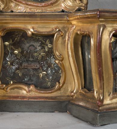 Zdjęcie nr 13: Feretron dwustronny z płaskorzeźbą Najświętszej Marii Panny Niepokalanie Poczętej na awersie oraz płaskorzeźbą ze sceną Narodzenia Najświętszej Marii Panny na rewersie, ustawiony na niskim postumencie o fantazyjnym wykroju z osią główną wysuniętą do przodu oraz narożnikami ustawionymi ukośnie. W postumencie dziewięć przeszklonych gablotek mieszczących relikwie świętych, które opisane są na małych karteczkach, otoczone różnego rodzaju kwiatkami  i gwiazdkami wykonanymi z papieru i cienkich blaszek. Otwory gablotek  o różnorodnym, fantazyjnym, opływowym wykroju. Na górnej powierzchni podstawy, po bokach małe otwory po zatkniętych w nich, niezachowanych rzeźbach apostołów. Rama obrazów w kształcie stojącego prostokąta, ujęta po każdej stronie trzema gablotkami otoczonymi rzeźbionym ornamentem rocaille'owym. W zwieńczeniu takie same, mniejsze gablotki, pośrodku zamiast relikwii owalna plakietka z kości z przedstawieniem Ucieczki do Egiptu. W zwieńczeniu na obłokach dwa aniołki podtrzymujące koronę. Na rewersie struktura feretronu o takim samym kształcie. Podstawa zdobiona gęstą wicią ze stylizowanych liści akantu zamkniętą w kształcie prostokąta leżącego.  Po bokach zamiast gablotek owoidalne pola, w których znajduje się złocona, drobna kratka.  W zwieńczeniu, w polu środkowym monogram Marii, powyżej aniołki trzymające koronę widoczne od tyłu.

Na awersie płaskorzeźba z przedstawieniem Najświętszej Marii Panny Niepokalanie Poczętej. Maria ukazana w postawie stojącej, frontalnie, na półksiężycu  i globie ziemskim, depcząca bosymi stopami węża, ze złożonymi w geście modlitwy rękami, z głową delikatnie przechyloną w prawą stronę. Twarz owalna z małymi i wąskimi ustami, wzrokiem skierowanym w dal. Włosy jasnobrązowe z przedziałkiem pośrodku, skryte pod płaszczem. Ubrana w długą, złoconą suknię z długimi rękawami, przewiązaną pod biustem oraz złoty płaszcz założony  na głowę i otulający całą postać, z lewym końcem przerzuconym przez prawe przedramię. W dolnej partii płaszcza oraz na prawej piersi ryta dekoracja roślinna, składająca się z sześciu ulistnionych gałązek z pięcio- lub sześciopłatkowymi kwiatkami. Wokół całej postaci Marii otok z srebrnych obłoków oraz promieni naprzemiennie prostych  i falujących. Wokół głowy złoty, kolisty nimb z gęsto ułożonych promieni; na nim okrąg z gwiazd dwunastu, częściowo nie zachowany. Tło srebrne, zdobione złoconą  i płaskorzeźbioną wicią z liści stylizujących suchy akant.

Na rewersie płaskorzeźba z przedstawieniem Narodzenia Najświętszej Marii Panny. Kompozycja dwustrefowa, w dolnej partii ukazani św. Joachim i św. Anna, w górnej Bóg Ojciec i Matka Boska w otoczeniu uskrzydlonych główek anielskich. Rodzice Marii w pozycji klęczącej, zwróceni trzy czwarte  ku środkowi. Ubrani w długie i złocone suknie z długimi rękawami oraz złote płaszcze, św. Anna z welonem na głowie. Pomiędzy nimi ustawiona ukośnie kołyska, ozdobiona na narożu uskrzydloną główką aniołka, przykryta długą tkaniną. U nóg św. Anny zamknięta księga, na obwolucie zdobiona prostym, łacińskim krzyżykiem. Po prawej stronie obrazu, za św. Anną, na wysokim postumencie antykizujący dzban. W górnej partii kompozycji Bóg Ojciec widoczny w półpostaci, frontalnie,  w lewym ręku trzymający jabłko królewskie, prawą wyciągający ku Marii. Ubrany  w złotą szatę z długimi rękawami oraz złoty płaszcz z rozwianym jednym końcem  po jego prawej stronie, wokół głowy złoty i trójkątny nimb. Twarz okolona gęstą i siwą brodą oraz siwymi, średniej długości włosami. Maria ukazana poniżej Boga Ojca,  w młodzieńczym wieku, w postawie stojącej na półksiężycu, frontalnie, z rękami złożonymi w geście modlitwy. Ubrana w długą i złotą suknię z długimi rękawami oraz złoty płaszcz, którego koniec przerzucony przez lewe ramię; wokół głowy złoty okrągły nimb. Włosy długie i jasnobrązowe, opadające na plecy. Tło utworzone  z obłoków. Wokół Boga Ojca i Marii cztery uskrzydlone główki aniołków o wyraźnie zaznaczonych pucułowatych policzkach. 

Relikwie  świętych umieszczone w niewielkich gablotkach za szybkami, opisane na karteczkach. Zwieńczenie feretronu, od lewej: nierozpoznane relikwie świętego, plakietka z kości  z przedstawieniem Ucieczki do Egiptu, relikwie „Sancta THERESIA Virgo”  Prawy bok feretronu, od góry: relikwie „Sanctae Katarzyny Panny”, relikwie „Sanctae Rozalii Panny”, relikwie „Sancta Illuminata Martir”. Podstawa feretronu, od lewej: relikwie „Sanctus Benedicti Martyr, Sancta Victoria Virgo Martyr, Sancti Floryana Męczennika”; relikwie „Sanctae Marciana Virgo Martyr”; relikwie  „Sanctus Quirini Martir”; relikwie „Sancti Jucundina Martyr”; relikwie „Sanctus Mansueti M.,  Sancta Eugenia Virgo Martyr, Sanctae Bronisławy”. Lewy bok feretronu, od góry: relikwie „Sanctus Jana Kantego”, relikwie „Sanctae Honorati Martyr”, relikwie „Sancta Illuminata Martir”. Plakietka ze sceną ucieczki do Egiptu o kształcie owalnym. W centrum kompozycji ukazani św. Józef oraz Maria z Dzieciątkiem Jezus na osiołku. Wokół słabo czytelny napis: „Cetur doms(e) in aeg vivo[?].” Rzeźby aniołków w zwieńczeniu usytuowane przeciwstawnie, diagonalnie, zwrócone górną partią ciała ku środkowi, jedną ręką podtrzymujące koronę. Ubrane w wąską tkaninę przerzuconą przez jedno z ramion i zwiewnie opadającą w dół. Korona w typie zamkniętym. Struktura feretronu złocona i srebrzona.	