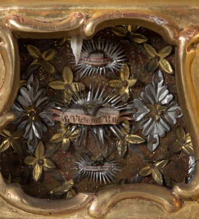 Zdjęcie nr 15: Feretron dwustronny z płaskorzeźbą Najświętszej Marii Panny Niepokalanie Poczętej na awersie oraz płaskorzeźbą ze sceną Narodzenia Najświętszej Marii Panny na rewersie, ustawiony na niskim postumencie o fantazyjnym wykroju z osią główną wysuniętą do przodu oraz narożnikami ustawionymi ukośnie. W postumencie dziewięć przeszklonych gablotek mieszczących relikwie świętych, które opisane są na małych karteczkach, otoczone różnego rodzaju kwiatkami  i gwiazdkami wykonanymi z papieru i cienkich blaszek. Otwory gablotek  o różnorodnym, fantazyjnym, opływowym wykroju. Na górnej powierzchni podstawy, po bokach małe otwory po zatkniętych w nich, niezachowanych rzeźbach apostołów. Rama obrazów w kształcie stojącego prostokąta, ujęta po każdej stronie trzema gablotkami otoczonymi rzeźbionym ornamentem rocaille&#039;owym. W zwieńczeniu takie same, mniejsze gablotki, pośrodku zamiast relikwii owalna plakietka z kości z przedstawieniem Ucieczki do Egiptu. W zwieńczeniu na obłokach dwa aniołki podtrzymujące koronę. Na rewersie struktura feretronu o takim samym kształcie. Podstawa zdobiona gęstą wicią ze stylizowanych liści akantu zamkniętą w kształcie prostokąta leżącego.  Po bokach zamiast gablotek owoidalne pola, w których znajduje się złocona, drobna kratka.  W zwieńczeniu, w polu środkowym monogram Marii, powyżej aniołki trzymające koronę widoczne od tyłu.

Na awersie płaskorzeźba z przedstawieniem Najświętszej Marii Panny Niepokalanie Poczętej. Maria ukazana w postawie stojącej, frontalnie, na półksiężycu  i globie ziemskim, depcząca bosymi stopami węża, ze złożonymi w geście modlitwy rękami, z głową delikatnie przechyloną w prawą stronę. Twarz owalna z małymi i wąskimi ustami, wzrokiem skierowanym w dal. Włosy jasnobrązowe z przedziałkiem pośrodku, skryte pod płaszczem. Ubrana w długą, złoconą suknię z długimi rękawami, przewiązaną pod biustem oraz złoty płaszcz założony  na głowę i otulający całą postać, z lewym końcem przerzuconym przez prawe przedramię. W dolnej partii płaszcza oraz na prawej piersi ryta dekoracja roślinna, składająca się z sześciu ulistnionych gałązek z pięcio- lub sześciopłatkowymi kwiatkami. Wokół całej postaci Marii otok z srebrnych obłoków oraz promieni naprzemiennie prostych  i falujących. Wokół głowy złoty, kolisty nimb z gęsto ułożonych promieni; na nim okrąg z gwiazd dwunastu, częściowo nie zachowany. Tło srebrne, zdobione złoconą  i płaskorzeźbioną wicią z liści stylizujących suchy akant.

Na rewersie płaskorzeźba z przedstawieniem Narodzenia Najświętszej Marii Panny. Kompozycja dwustrefowa, w dolnej partii ukazani św. Joachim i św. Anna, w górnej Bóg Ojciec i Matka Boska w otoczeniu uskrzydlonych główek anielskich. Rodzice Marii w pozycji klęczącej, zwróceni trzy czwarte  ku środkowi. Ubrani w długie i złocone suknie z długimi rękawami oraz złote płaszcze, św. Anna z welonem na głowie. Pomiędzy nimi ustawiona ukośnie kołyska, ozdobiona na narożu uskrzydloną główką aniołka, przykryta długą tkaniną. U nóg św. Anny zamknięta księga, na obwolucie zdobiona prostym, łacińskim krzyżykiem. Po prawej stronie obrazu, za św. Anną, na wysokim postumencie antykizujący dzban. W górnej partii kompozycji Bóg Ojciec widoczny w półpostaci, frontalnie,  w lewym ręku trzymający jabłko królewskie, prawą wyciągający ku Marii. Ubrany  w złotą szatę z długimi rękawami oraz złoty płaszcz z rozwianym jednym końcem  po jego prawej stronie, wokół głowy złoty i trójkątny nimb. Twarz okolona gęstą i siwą brodą oraz siwymi, średniej długości włosami. Maria ukazana poniżej Boga Ojca,  w młodzieńczym wieku, w postawie stojącej na półksiężycu, frontalnie, z rękami złożonymi w geście modlitwy. Ubrana w długą i złotą suknię z długimi rękawami oraz złoty płaszcz, którego koniec przerzucony przez lewe ramię; wokół głowy złoty okrągły nimb. Włosy długie i jasnobrązowe, opadające na plecy. Tło utworzone  z obłoków. Wokół Boga Ojca i Marii cztery uskrzydlone główki aniołków o wyraźnie zaznaczonych pucułowatych policzkach. 

Relikwie  świętych umieszczone w niewielkich gablotkach za szybkami, opisane na karteczkach. Zwieńczenie feretronu, od lewej: nierozpoznane relikwie świętego, plakietka z kości  z przedstawieniem Ucieczki do Egiptu, relikwie „Sancta THERESIA Virgo”  Prawy bok feretronu, od góry: relikwie „Sanctae Katarzyny Panny”, relikwie „Sanctae Rozalii Panny”, relikwie „Sancta Illuminata Martir”. Podstawa feretronu, od lewej: relikwie „Sanctus Benedicti Martyr, Sancta Victoria Virgo Martyr, Sancti Floryana Męczennika”; relikwie „Sanctae Marciana Virgo Martyr”; relikwie  „Sanctus Quirini Martir”; relikwie „Sancti Jucundina Martyr”; relikwie „Sanctus Mansueti M.,  Sancta Eugenia Virgo Martyr, Sanctae Bronisławy”. Lewy bok feretronu, od góry: relikwie „Sanctus Jana Kantego”, relikwie „Sanctae Honorati Martyr”, relikwie „Sancta Illuminata Martir”. Plakietka ze sceną ucieczki do Egiptu o kształcie owalnym. W centrum kompozycji ukazani św. Józef oraz Maria z Dzieciątkiem Jezus na osiołku. Wokół słabo czytelny napis: „Cetur doms(e) in aeg vivo[?].” Rzeźby aniołków w zwieńczeniu usytuowane przeciwstawnie, diagonalnie, zwrócone górną partią ciała ku środkowi, jedną ręką podtrzymujące koronę. Ubrane w wąską tkaninę przerzuconą przez jedno z ramion i zwiewnie opadającą w dół. Korona w typie zamkniętym. Struktura feretronu złocona i srebrzona.	