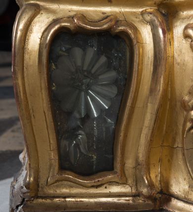 Zdjęcie nr 18: Feretron dwustronny z płaskorzeźbą Najświętszej Marii Panny Niepokalanie Poczętej na awersie oraz płaskorzeźbą ze sceną Narodzenia Najświętszej Marii Panny na rewersie, ustawiony na niskim postumencie o fantazyjnym wykroju z osią główną wysuniętą do przodu oraz narożnikami ustawionymi ukośnie. W postumencie dziewięć przeszklonych gablotek mieszczących relikwie świętych, które opisane są na małych karteczkach, otoczone różnego rodzaju kwiatkami  i gwiazdkami wykonanymi z papieru i cienkich blaszek. Otwory gablotek  o różnorodnym, fantazyjnym, opływowym wykroju. Na górnej powierzchni podstawy, po bokach małe otwory po zatkniętych w nich, niezachowanych rzeźbach apostołów. Rama obrazów w kształcie stojącego prostokąta, ujęta po każdej stronie trzema gablotkami otoczonymi rzeźbionym ornamentem rocaille&#039;owym. W zwieńczeniu takie same, mniejsze gablotki, pośrodku zamiast relikwii owalna plakietka z kości z przedstawieniem Ucieczki do Egiptu. W zwieńczeniu na obłokach dwa aniołki podtrzymujące koronę. Na rewersie struktura feretronu o takim samym kształcie. Podstawa zdobiona gęstą wicią ze stylizowanych liści akantu zamkniętą w kształcie prostokąta leżącego.  Po bokach zamiast gablotek owoidalne pola, w których znajduje się złocona, drobna kratka.  W zwieńczeniu, w polu środkowym monogram Marii, powyżej aniołki trzymające koronę widoczne od tyłu.

Na awersie płaskorzeźba z przedstawieniem Najświętszej Marii Panny Niepokalanie Poczętej. Maria ukazana w postawie stojącej, frontalnie, na półksiężycu  i globie ziemskim, depcząca bosymi stopami węża, ze złożonymi w geście modlitwy rękami, z głową delikatnie przechyloną w prawą stronę. Twarz owalna z małymi i wąskimi ustami, wzrokiem skierowanym w dal. Włosy jasnobrązowe z przedziałkiem pośrodku, skryte pod płaszczem. Ubrana w długą, złoconą suknię z długimi rękawami, przewiązaną pod biustem oraz złoty płaszcz założony  na głowę i otulający całą postać, z lewym końcem przerzuconym przez prawe przedramię. W dolnej partii płaszcza oraz na prawej piersi ryta dekoracja roślinna, składająca się z sześciu ulistnionych gałązek z pięcio- lub sześciopłatkowymi kwiatkami. Wokół całej postaci Marii otok z srebrnych obłoków oraz promieni naprzemiennie prostych  i falujących. Wokół głowy złoty, kolisty nimb z gęsto ułożonych promieni; na nim okrąg z gwiazd dwunastu, częściowo nie zachowany. Tło srebrne, zdobione złoconą  i płaskorzeźbioną wicią z liści stylizujących suchy akant.

Na rewersie płaskorzeźba z przedstawieniem Narodzenia Najświętszej Marii Panny. Kompozycja dwustrefowa, w dolnej partii ukazani św. Joachim i św. Anna, w górnej Bóg Ojciec i Matka Boska w otoczeniu uskrzydlonych główek anielskich. Rodzice Marii w pozycji klęczącej, zwróceni trzy czwarte  ku środkowi. Ubrani w długie i złocone suknie z długimi rękawami oraz złote płaszcze, św. Anna z welonem na głowie. Pomiędzy nimi ustawiona ukośnie kołyska, ozdobiona na narożu uskrzydloną główką aniołka, przykryta długą tkaniną. U nóg św. Anny zamknięta księga, na obwolucie zdobiona prostym, łacińskim krzyżykiem. Po prawej stronie obrazu, za św. Anną, na wysokim postumencie antykizujący dzban. W górnej partii kompozycji Bóg Ojciec widoczny w półpostaci, frontalnie,  w lewym ręku trzymający jabłko królewskie, prawą wyciągający ku Marii. Ubrany  w złotą szatę z długimi rękawami oraz złoty płaszcz z rozwianym jednym końcem  po jego prawej stronie, wokół głowy złoty i trójkątny nimb. Twarz okolona gęstą i siwą brodą oraz siwymi, średniej długości włosami. Maria ukazana poniżej Boga Ojca,  w młodzieńczym wieku, w postawie stojącej na półksiężycu, frontalnie, z rękami złożonymi w geście modlitwy. Ubrana w długą i złotą suknię z długimi rękawami oraz złoty płaszcz, którego koniec przerzucony przez lewe ramię; wokół głowy złoty okrągły nimb. Włosy długie i jasnobrązowe, opadające na plecy. Tło utworzone  z obłoków. Wokół Boga Ojca i Marii cztery uskrzydlone główki aniołków o wyraźnie zaznaczonych pucułowatych policzkach. 

Relikwie  świętych umieszczone w niewielkich gablotkach za szybkami, opisane na karteczkach. Zwieńczenie feretronu, od lewej: nierozpoznane relikwie świętego, plakietka z kości  z przedstawieniem Ucieczki do Egiptu, relikwie „Sancta THERESIA Virgo”  Prawy bok feretronu, od góry: relikwie „Sanctae Katarzyny Panny”, relikwie „Sanctae Rozalii Panny”, relikwie „Sancta Illuminata Martir”. Podstawa feretronu, od lewej: relikwie „Sanctus Benedicti Martyr, Sancta Victoria Virgo Martyr, Sancti Floryana Męczennika”; relikwie „Sanctae Marciana Virgo Martyr”; relikwie  „Sanctus Quirini Martir”; relikwie „Sancti Jucundina Martyr”; relikwie „Sanctus Mansueti M.,  Sancta Eugenia Virgo Martyr, Sanctae Bronisławy”. Lewy bok feretronu, od góry: relikwie „Sanctus Jana Kantego”, relikwie „Sanctae Honorati Martyr”, relikwie „Sancta Illuminata Martir”. Plakietka ze sceną ucieczki do Egiptu o kształcie owalnym. W centrum kompozycji ukazani św. Józef oraz Maria z Dzieciątkiem Jezus na osiołku. Wokół słabo czytelny napis: „Cetur doms(e) in aeg vivo[?].” Rzeźby aniołków w zwieńczeniu usytuowane przeciwstawnie, diagonalnie, zwrócone górną partią ciała ku środkowi, jedną ręką podtrzymujące koronę. Ubrane w wąską tkaninę przerzuconą przez jedno z ramion i zwiewnie opadającą w dół. Korona w typie zamkniętym. Struktura feretronu złocona i srebrzona.	