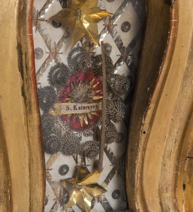 Zdjęcie nr 11: Feretron dwustronny  z obrazami świętej Anny Samotrzeć oraz św. Jana Kantego adorującego Matkę Boską  z Dzieciątkiem ustawiony na niskim postumencie o fantazyjnym kształcie z osią główną wysuniętą do przodu oraz narożnikami ustawionymi ukośnie.  W postumencie dziewięć przeszklonych gablotek mieszczących relikwie świętych, które opisane są na małych karteczkach, otoczone różnego rodzaju kwiatkami  i gwiazdkami wykonanymi z papieru i cienkich blaszek. Otwory gablotek  o różnorodnym, opływowym wykroju. Po bokach, na górnej powierzchni podstawy małe otwory po zatkniętych w nich, niezachowanych rzeźbach apostołów. Rama  w kształcie stojącego prostokąta, ujęta po każdej stronie trzema gablotkami otoczonymi rzeźbionym ornamentem rocaille'owym. W zwieńczeniu takie same, mniejsze gablotki, pośrodku zamiast relikwii ażurowa, rzeźbiona wić roślinna. Na rewersie struktura feretronu o takim samym kształcie. Podstawa zdobiona siedmioma ramkami  o fantazyjnym kształtach utworzonych z wąskich esownic. Po bokach zamiast gablotek  owoidalne pola, w których złocona, drobna kratka. Rama zdobiona ornamentem rocaille'owym.

Na awersie obraz z przedstawieniem św. Anny Samotrzeć. W centrum kompozycji ukazane są w postawie siedzącej św. Anna po prawej stronie i Matka Boska z Dzieciątkiem Jezus po lewej stronie. Maria zwrócona trzy czwarte w lewo, rękami przytrzymująca siedzące na jej kolanach Dzieciątko. Twarz owalna, z wyraźnie zaznaczonym podbródkiem, małe i jasnoróżowe usta, długi i szeroki nos, oczy lekko przymknięte, wysokie czoło. Włosy długie, falowane, z przedziałkiem pośrodku opadające na plecy i prawe ramię. Ubrana jest w długą, różową suknię ze złotym obszyciem pod szyją i na rękawach; niebieski płaszcz z brązową podszewką, zarzucony na plecy i otulający kolana oraz biały, delikatny welon  na głowie. Dzieciątko Jezus ukazane jest frontalnie, z lewą rączką uniesioną w geście błogosławieństwa. Twarz szeroka  z długim i szerokim nosem, wysokim czołem. Włosy krótkie, jasne, kędzierzawe. Wokół bioder ma założoną białą pieluszkę. Święta Anna zwrócona trzy czwarte w prawo,  z głową widoczną z lewego profilu, z lewą ręką przytrzymująca lewą rączkę Dzieciątka. Twarz podłużna z długim i szerokim nosem. Ubrana jest w długą zieloną suknię z długimi rękawami, czerwony płaszcz przerzucony  przez prawe ramię i zasłaniający kolana oraz jasnobrązową chustę zakrywającą włosy  i szyję. Karnacja ciemna. Wokół głów postaci złote, okrągłe nimby. W dolnej części obrazu widoczna roślinność, w górnej szarobłękitne niebo.

Na rewersie obraz z przedstawieniem Matki Boskiej z Dzieciątkiem adorowanych przez św. Jana Kantego. Scena zakomponowana  w architektonicznym wnętrzu. Maria ukazana w lewym górnym narożu obrazu,  w pozycji siedzącej na obłoku, zwrócona trzy czwarte w lewo, rękami przytrzymująca stojące na jej kolanach Dzieciątko. Twarz owalna z długim i wąskim nosem. Włosy długie, kręcone, ciemnobrązowe, schowane pod chustą. Ubrana w jasnoróżową suknię z długimi rękawami, niebieski płaszcz zasłaniający kolana, brązową chustę na głowie; na stopach sandały. Dzieciątko ukazane w pozycji stojącej, z lewą rączką wyciągniętą przed siebie, otulone przez Marię białą chustą na wysokości bioder. Diagonalnie, w dolnym, prawym narożu obrazu ukazany św. Jan Kanty; zwrócony trzy czwarte w prawo; z rękami wzniesionymi w geście modlitwy; z głową widoczną z lewego profilu, zwróconą w stronę Marii. Ubrany jest w togę profesorską. Twarz podłużna z długim i wąskim nosem, okolona krótko przystrzyżoną, siwą brodą. Włosy średniej długości, zwinięte w siwe pukle. Wokół głowy złoty, okrągły nimb. W dolnym narożu obrazu, na kamiennej posadzce otwarta, zapisana księga oraz zielona palma. Tło architektoniczne, po prawej stronie widoczna ostrołukowa arkada.

Relikwie umieszczone w niewielkich wnękach, za szybkami, opisane. Zwieńczenie feretronu, od lewej: relikwie „Sancti Vincentii Martyr”, relikwie „Sanctae Perpentuae Martyr”. Prawy bok feretronu, od góry: relikwie „Sancti Longina Męczennika”; relikwie  „Sanctae Kunegundy Panny”; relikwie „Mafsa SS. MM.”, „Sanctae Victorii Martyr”, „Sanctae Agnészki Panny i [...]”. Podstawa feretronu, od lewej: relikwie „Sancti Grzegorza Papieża”; relikwie „Sanctae Katarzyny”; relikwie „sanctus Clarus martyr”; relikwie „Sanctae Theogeni Martyr”; relikwie  „Sancti Urbana Papieża, Pluvium. Mino., Świętych Męczenników, Sanctae Gratii Marii”; relikwie „Sancti Theodori Martyr.”; relikwie „Sancti Jucundi Martyr”; relikwie „Iňocentii XI.”; relikwie „Sancti Jana Kapistrana”. Lewy bok feretronu, od góry: relikwie „Sancti Jana Kantego”; relikwie  „Sanctae Jadwigi Polki”; relikwie „Sanctae Pauliny Panny Męczennicy, Sancti Celestyna Papieża Męczen.,  SANCTI STANISŁAWA BISKUPA I MĘCZENNIKA”.
