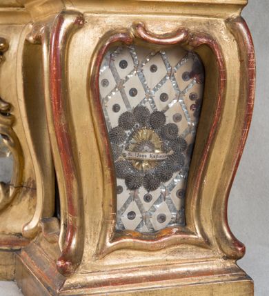 Zdjęcie nr 27: Feretron dwustronny  z obrazami świętej Anny Samotrzeć oraz św. Jana Kantego adorującego Matkę Boską  z Dzieciątkiem ustawiony na niskim postumencie o fantazyjnym kształcie z osią główną wysuniętą do przodu oraz narożnikami ustawionymi ukośnie.  W postumencie dziewięć przeszklonych gablotek mieszczących relikwie świętych, które opisane są na małych karteczkach, otoczone różnego rodzaju kwiatkami  i gwiazdkami wykonanymi z papieru i cienkich blaszek. Otwory gablotek  o różnorodnym, opływowym wykroju. Po bokach, na górnej powierzchni podstawy małe otwory po zatkniętych w nich, niezachowanych rzeźbach apostołów. Rama  w kształcie stojącego prostokąta, ujęta po każdej stronie trzema gablotkami otoczonymi rzeźbionym ornamentem rocaille&#039;owym. W zwieńczeniu takie same, mniejsze gablotki, pośrodku zamiast relikwii ażurowa, rzeźbiona wić roślinna. Na rewersie struktura feretronu o takim samym kształcie. Podstawa zdobiona siedmioma ramkami  o fantazyjnym kształtach utworzonych z wąskich esownic. Po bokach zamiast gablotek  owoidalne pola, w których złocona, drobna kratka. Rama zdobiona ornamentem rocaille&#039;owym.

Na awersie obraz z przedstawieniem św. Anny Samotrzeć. W centrum kompozycji ukazane są w postawie siedzącej św. Anna po prawej stronie i Matka Boska z Dzieciątkiem Jezus po lewej stronie. Maria zwrócona trzy czwarte w lewo, rękami przytrzymująca siedzące na jej kolanach Dzieciątko. Twarz owalna, z wyraźnie zaznaczonym podbródkiem, małe i jasnoróżowe usta, długi i szeroki nos, oczy lekko przymknięte, wysokie czoło. Włosy długie, falowane, z przedziałkiem pośrodku opadające na plecy i prawe ramię. Ubrana jest w długą, różową suknię ze złotym obszyciem pod szyją i na rękawach; niebieski płaszcz z brązową podszewką, zarzucony na plecy i otulający kolana oraz biały, delikatny welon  na głowie. Dzieciątko Jezus ukazane jest frontalnie, z lewą rączką uniesioną w geście błogosławieństwa. Twarz szeroka  z długim i szerokim nosem, wysokim czołem. Włosy krótkie, jasne, kędzierzawe. Wokół bioder ma założoną białą pieluszkę. Święta Anna zwrócona trzy czwarte w prawo,  z głową widoczną z lewego profilu, z lewą ręką przytrzymująca lewą rączkę Dzieciątka. Twarz podłużna z długim i szerokim nosem. Ubrana jest w długą zieloną suknię z długimi rękawami, czerwony płaszcz przerzucony  przez prawe ramię i zasłaniający kolana oraz jasnobrązową chustę zakrywającą włosy  i szyję. Karnacja ciemna. Wokół głów postaci złote, okrągłe nimby. W dolnej części obrazu widoczna roślinność, w górnej szarobłękitne niebo.

Na rewersie obraz z przedstawieniem Matki Boskiej z Dzieciątkiem adorowanych przez św. Jana Kantego. Scena zakomponowana  w architektonicznym wnętrzu. Maria ukazana w lewym górnym narożu obrazu,  w pozycji siedzącej na obłoku, zwrócona trzy czwarte w lewo, rękami przytrzymująca stojące na jej kolanach Dzieciątko. Twarz owalna z długim i wąskim nosem. Włosy długie, kręcone, ciemnobrązowe, schowane pod chustą. Ubrana w jasnoróżową suknię z długimi rękawami, niebieski płaszcz zasłaniający kolana, brązową chustę na głowie; na stopach sandały. Dzieciątko ukazane w pozycji stojącej, z lewą rączką wyciągniętą przed siebie, otulone przez Marię białą chustą na wysokości bioder. Diagonalnie, w dolnym, prawym narożu obrazu ukazany św. Jan Kanty; zwrócony trzy czwarte w prawo; z rękami wzniesionymi w geście modlitwy; z głową widoczną z lewego profilu, zwróconą w stronę Marii. Ubrany jest w togę profesorską. Twarz podłużna z długim i wąskim nosem, okolona krótko przystrzyżoną, siwą brodą. Włosy średniej długości, zwinięte w siwe pukle. Wokół głowy złoty, okrągły nimb. W dolnym narożu obrazu, na kamiennej posadzce otwarta, zapisana księga oraz zielona palma. Tło architektoniczne, po prawej stronie widoczna ostrołukowa arkada.

Relikwie umieszczone w niewielkich wnękach, za szybkami, opisane. Zwieńczenie feretronu, od lewej: relikwie „Sancti Vincentii Martyr”, relikwie „Sanctae Perpentuae Martyr”. Prawy bok feretronu, od góry: relikwie „Sancti Longina Męczennika”; relikwie  „Sanctae Kunegundy Panny”; relikwie „Mafsa SS. MM.”, „Sanctae Victorii Martyr”, „Sanctae Agnészki Panny i [...]”. Podstawa feretronu, od lewej: relikwie „Sancti Grzegorza Papieża”; relikwie „Sanctae Katarzyny”; relikwie „sanctus Clarus martyr”; relikwie „Sanctae Theogeni Martyr”; relikwie  „Sancti Urbana Papieża, Pluvium. Mino., Świętych Męczenników, Sanctae Gratii Marii”; relikwie „Sancti Theodori Martyr.”; relikwie „Sancti Jucundi Martyr”; relikwie „Iňocentii XI.”; relikwie „Sancti Jana Kapistrana”. Lewy bok feretronu, od góry: relikwie „Sancti Jana Kantego”; relikwie  „Sanctae Jadwigi Polki”; relikwie „Sanctae Pauliny Panny Męczennicy, Sancti Celestyna Papieża Męczen.,  SANCTI STANISŁAWA BISKUPA I MĘCZENNIKA”.
