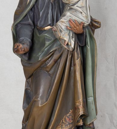 Zdjęcie nr 7: Feretron z rzeźbą św. Józefa z Dzieciątkiem ustawiony na wysokim postumencie. Postument zwężający się ku górze,  po  bokach flankowany dwiema wolutami, zaopatrzony w otwory na drążki do noszenia, stojący na czterech lwich łapkach. Na ściance frontowej zdobiony esownicami utworzonymi z liści akantu, kratką pośrodku oraz muszlą palmetową powyżej. Rzeźba ustawiona na niskim, kwadratowym, ciemnozielonym, cokole o ściętych narożach. Święty Józef ukazany w postawie stojącej, w delikatnym kontrapoście z Dzieciątkiem Jezus na lewym ręku, z prawą ręką wysuniętą przed siebie. Twarz podłużna, z długim i wąskim nosem, okolona krótko przystrzyżoną brodą; włosy brązowe, średniej długości, kręcone. Święty jest ubrany jest w ciemnofioletową suknię z długimi rękawami i ze złotą lamówką u dołu oraz przy szyi, przepasaną złotym paskiem; jasnobrązowy płaszcz z zieloną podszewką na brzegu zdobiony wicią roślinną  z owocami granatu; stopy bose. Dzieciątko Jezus ukazane w pozycji siedzącej na lewym ramieniu św. Józefa, prawą rączką obejmuje go za szyję, lewą kładzie na jego piersi. Twarz okrągła, wysokie czoło, małe usta, jasnobłękitne oczy, nos krótki i szeroki; włosy krótkie, jasne i kręcone. Dzieciątko jest ubrane w białą, długą sukienkę  z długimi rękawami, ze złotym obszyciem na brzegach, zdobioną malowanymi, złotymi małymi krzyżykami. Struktura postumentu polichromowana w kolorze jasnoszarym, detale  i ornamentyka złocone.
