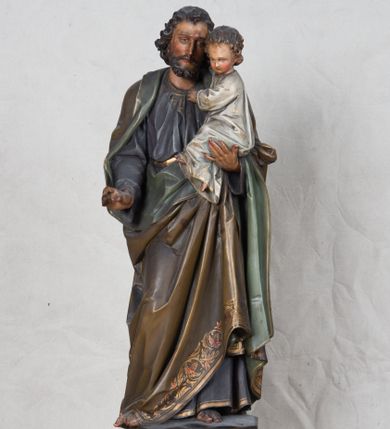 Zdjęcie nr 1: Feretron z rzeźbą św. Józefa z Dzieciątkiem ustawiony na wysokim postumencie. Postument zwężający się ku górze,  po  bokach flankowany dwiema wolutami, zaopatrzony w otwory na drążki do noszenia, stojący na czterech lwich łapkach. Na ściance frontowej zdobiony esownicami utworzonymi z liści akantu, kratką pośrodku oraz muszlą palmetową powyżej. Rzeźba ustawiona na niskim, kwadratowym, ciemnozielonym, cokole o ściętych narożach. Święty Józef ukazany w postawie stojącej, w delikatnym kontrapoście z Dzieciątkiem Jezus na lewym ręku, z prawą ręką wysuniętą przed siebie. Twarz podłużna, z długim i wąskim nosem, okolona krótko przystrzyżoną brodą; włosy brązowe, średniej długości, kręcone. Święty jest ubrany jest w ciemnofioletową suknię z długimi rękawami i ze złotą lamówką u dołu oraz przy szyi, przepasaną złotym paskiem; jasnobrązowy płaszcz z zieloną podszewką na brzegu zdobiony wicią roślinną  z owocami granatu; stopy bose. Dzieciątko Jezus ukazane w pozycji siedzącej na lewym ramieniu św. Józefa, prawą rączką obejmuje go za szyję, lewą kładzie na jego piersi. Twarz okrągła, wysokie czoło, małe usta, jasnobłękitne oczy, nos krótki i szeroki; włosy krótkie, jasne i kręcone. Dzieciątko jest ubrane w białą, długą sukienkę  z długimi rękawami, ze złotym obszyciem na brzegach, zdobioną malowanymi, złotymi małymi krzyżykami. Struktura postumentu polichromowana w kolorze jasnoszarym, detale  i ornamentyka złocone.

