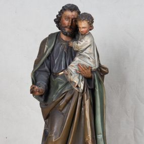 Zdjęcie nr 1: Feretron z rzeźbą św. Józefa z Dzieciątkiem ustawiony na wysokim postumencie. Postument zwężający się ku górze,  po  bokach flankowany dwiema wolutami, zaopatrzony w otwory na drążki do noszenia, stojący na czterech lwich łapkach. Na ściance frontowej zdobiony esownicami utworzonymi z liści akantu, kratką pośrodku oraz muszlą palmetową powyżej. Rzeźba ustawiona na niskim, kwadratowym, ciemnozielonym, cokole o ściętych narożach. Święty Józef ukazany w postawie stojącej, w delikatnym kontrapoście z Dzieciątkiem Jezus na lewym ręku, z prawą ręką wysuniętą przed siebie. Twarz podłużna, z długim i wąskim nosem, okolona krótko przystrzyżoną brodą; włosy brązowe, średniej długości, kręcone. Święty jest ubrany jest w ciemnofioletową suknię z długimi rękawami i ze złotą lamówką u dołu oraz przy szyi, przepasaną złotym paskiem; jasnobrązowy płaszcz z zieloną podszewką na brzegu zdobiony wicią roślinną  z owocami granatu; stopy bose. Dzieciątko Jezus ukazane w pozycji siedzącej na lewym ramieniu św. Józefa, prawą rączką obejmuje go za szyję, lewą kładzie na jego piersi. Twarz okrągła, wysokie czoło, małe usta, jasnobłękitne oczy, nos krótki i szeroki; włosy krótkie, jasne i kręcone. Dzieciątko jest ubrane w białą, długą sukienkę  z długimi rękawami, ze złotym obszyciem na brzegach, zdobioną malowanymi, złotymi małymi krzyżykami. Struktura postumentu polichromowana w kolorze jasnoszarym, detale  i ornamentyka złocone.
