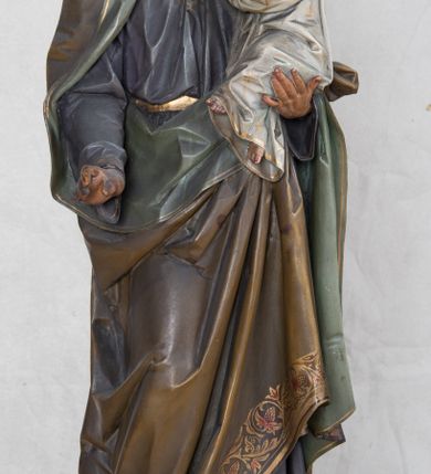 Zdjęcie nr 9: Feretron z rzeźbą św. Józefa z Dzieciątkiem ustawiony na wysokim postumencie. Postument zwężający się ku górze,  po  bokach flankowany dwiema wolutami, zaopatrzony w otwory na drążki do noszenia, stojący na czterech lwich łapkach. Na ściance frontowej zdobiony esownicami utworzonymi z liści akantu, kratką pośrodku oraz muszlą palmetową powyżej. Rzeźba ustawiona na niskim, kwadratowym, ciemnozielonym, cokole o ściętych narożach. Święty Józef ukazany w postawie stojącej, w delikatnym kontrapoście z Dzieciątkiem Jezus na lewym ręku, z prawą ręką wysuniętą przed siebie. Twarz podłużna, z długim i wąskim nosem, okolona krótko przystrzyżoną brodą; włosy brązowe, średniej długości, kręcone. Święty jest ubrany jest w ciemnofioletową suknię z długimi rękawami i ze złotą lamówką u dołu oraz przy szyi, przepasaną złotym paskiem; jasnobrązowy płaszcz z zieloną podszewką na brzegu zdobiony wicią roślinną  z owocami granatu; stopy bose. Dzieciątko Jezus ukazane w pozycji siedzącej na lewym ramieniu św. Józefa, prawą rączką obejmuje go za szyję, lewą kładzie na jego piersi. Twarz okrągła, wysokie czoło, małe usta, jasnobłękitne oczy, nos krótki i szeroki; włosy krótkie, jasne i kręcone. Dzieciątko jest ubrane w białą, długą sukienkę  z długimi rękawami, ze złotym obszyciem na brzegach, zdobioną malowanymi, złotymi małymi krzyżykami. Struktura postumentu polichromowana w kolorze jasnoszarym, detale  i ornamentyka złocone.
