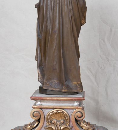 Zdjęcie nr 6: Feretron z rzeźbą św. Józefa z Dzieciątkiem ustawiony na wysokim postumencie. Postument zwężający się ku górze,  po  bokach flankowany dwiema wolutami, zaopatrzony w otwory na drążki do noszenia, stojący na czterech lwich łapkach. Na ściance frontowej zdobiony esownicami utworzonymi z liści akantu, kratką pośrodku oraz muszlą palmetową powyżej. Rzeźba ustawiona na niskim, kwadratowym, ciemnozielonym, cokole o ściętych narożach. Święty Józef ukazany w postawie stojącej, w delikatnym kontrapoście z Dzieciątkiem Jezus na lewym ręku, z prawą ręką wysuniętą przed siebie. Twarz podłużna, z długim i wąskim nosem, okolona krótko przystrzyżoną brodą; włosy brązowe, średniej długości, kręcone. Święty jest ubrany jest w ciemnofioletową suknię z długimi rękawami i ze złotą lamówką u dołu oraz przy szyi, przepasaną złotym paskiem; jasnobrązowy płaszcz z zieloną podszewką na brzegu zdobiony wicią roślinną  z owocami granatu; stopy bose. Dzieciątko Jezus ukazane w pozycji siedzącej na lewym ramieniu św. Józefa, prawą rączką obejmuje go za szyję, lewą kładzie na jego piersi. Twarz okrągła, wysokie czoło, małe usta, jasnobłękitne oczy, nos krótki i szeroki; włosy krótkie, jasne i kręcone. Dzieciątko jest ubrane w białą, długą sukienkę  z długimi rękawami, ze złotym obszyciem na brzegach, zdobioną malowanymi, złotymi małymi krzyżykami. Struktura postumentu polichromowana w kolorze jasnoszarym, detale  i ornamentyka złocone.
