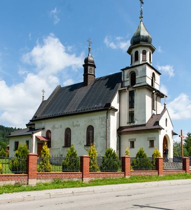 Zdjęcie nr 8: Kościół Niepokalanego Serca Najświętszej Marii Panny w Hucisku usytuowany jest w południowo-zachodniej części wsi. Plac przykościelny otoczony jest żeliwnym płotem z murowanymi słupkami. Kościół skierowany jest na zachód, murowany, otynkowany z wieżą od wschodu. Wnętrze świątyni tworzy niewielkie, prostokątne, prezbiterium zakończone trójbocznie. Nawa jest szersza, na planie prostokąta, nakryta stropem, oddzielona od prezbiterium szeroką, półkoliście zamkniętą arkadą w ścianie tęczowej. Od południa do prezbiterium przylega założona na planie prostokąta niewielka zakrystia. Na wschodniej ścianie kościoła drewniany chór muzyczny, wsparty na dwóch filarach jest dostępny schodami od południowej strony nawy. Nawę oświetlają umieszczone w północnych i południowych ścianach prostokątne, zamknięte półkoliście okna, po trzy z każdej strony. Do świątyni prowadzą dwa wejścia: główne od strony wschodniej, drugie przez zakrystię. Wejście główne prowadzi poprzez dwuskrzydłowe drzwi z kruchty pod wieżą. 

W zewnętrznej elewacji kościoła widoczny jest niewysoki, kamienny cokół, wykonany z regularnych ciosów kamienia. Prezbiterium jest niższe od nawy. Do wschodniej fasady kościoła dostawiono założoną na planie kwadratu dwukondygnacyjną wieżę-dzwonnicę, ustawioną na kruchcie na planie prostokąta. Kruchta została zamknięta trójkątnym szczytem; w jej polu znajduje się głęboka wnęka w kształcie stojącego prostokąta, zamknięta łukiem półkolistym. Poszczególne kondygnacje wieży rozdzielone są daszkami i przeprute otworami okiennymi. Całość zwieńczono wieloboczną latarnią oraz cebulastym hełmem z łacińskim krzyżem. Prezbiterium i nawa przykryte są oddzielnie, stromymi dachami dwuspadowymi. Na środku nawy znajduje się wieżyczka na sygnaturkę z latarnią i cebulastym hełmem. 