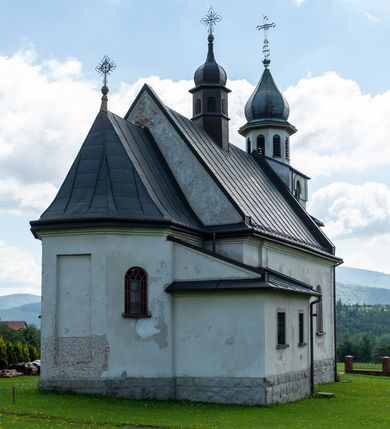 Zdjęcie nr 11: Kościół Niepokalanego Serca Najświętszej Marii Panny w Hucisku usytuowany jest w południowo-zachodniej części wsi. Plac przykościelny otoczony jest żeliwnym płotem z murowanymi słupkami. Kościół skierowany jest na zachód, murowany, otynkowany z wieżą od wschodu. Wnętrze świątyni tworzy niewielkie, prostokątne, prezbiterium zakończone trójbocznie. Nawa jest szersza, na planie prostokąta, nakryta stropem, oddzielona od prezbiterium szeroką, półkoliście zamkniętą arkadą w ścianie tęczowej. Od południa do prezbiterium przylega założona na planie prostokąta niewielka zakrystia. Na wschodniej ścianie kościoła drewniany chór muzyczny, wsparty na dwóch filarach jest dostępny schodami od południowej strony nawy. Nawę oświetlają umieszczone w północnych i południowych ścianach prostokątne, zamknięte półkoliście okna, po trzy z każdej strony. Do świątyni prowadzą dwa wejścia: główne od strony wschodniej, drugie przez zakrystię. Wejście główne prowadzi poprzez dwuskrzydłowe drzwi z kruchty pod wieżą. 

W zewnętrznej elewacji kościoła widoczny jest niewysoki, kamienny cokół, wykonany z regularnych ciosów kamienia. Prezbiterium jest niższe od nawy. Do wschodniej fasady kościoła dostawiono założoną na planie kwadratu dwukondygnacyjną wieżę-dzwonnicę, ustawioną na kruchcie na planie prostokąta. Kruchta została zamknięta trójkątnym szczytem; w jej polu znajduje się głęboka wnęka w kształcie stojącego prostokąta, zamknięta łukiem półkolistym. Poszczególne kondygnacje wieży rozdzielone są daszkami i przeprute otworami okiennymi. Całość zwieńczono wieloboczną latarnią oraz cebulastym hełmem z łacińskim krzyżem. Prezbiterium i nawa przykryte są oddzielnie, stromymi dachami dwuspadowymi. Na środku nawy znajduje się wieżyczka na sygnaturkę z latarnią i cebulastym hełmem. 