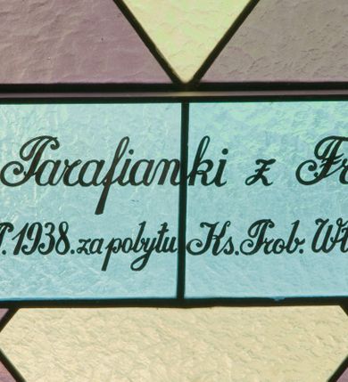 Zdjęcie nr 3: Witraż w kształcie stojącego prostokąta zamkniętego łukiem półkolistym ujęty geometryczną bordiurą wypełnioną motywem białych i niebieskich trójkątów oraz ciemnoczerwonych rombów. W polu ukośna kratka wypełniona ułożonymi naprzemiennie białymi i jasnofioletowymi rombami. W dolnej części witraża owalny medalion wsparty na girlandzie białych, kwitnących róż mieszczący popiersie Matki Boskiej z Dzieciątkiem ukazanej w typie Matki Boskiej Nieustającej Pomocy umieszczone na złotym tle. Maria zwrócona w trzech czwartych w lewo, na lewym przedramieniu trzyma siedzące Dzieciątko, prawą dłonią podtrzymuje dłonie Jezusa. Matka Boska ubrana jest w czerwoną suknię z długimi rękawami wykończoną przy dekolcie złotą lamówką oraz niebieski płaszcz zarzucony na głowę. Dzieciątko jest zwrócone w trzech czwartych w prawo z głową w przeciwnym kierunku. Jezus nosi jasnozieloną tunikę z długimi, szerokimi rękawami oraz złoty, szrafowany płaszcz, spod którego widoczne są bose stopy. Wokół głowy Marii znajduje się biały nimb wypełniony bordiurą roślinną, wokół głowy Dzieciątka nimb krzyżowy. Obie postaci ukazane są w złotych, kameryzowanych koronach typu otwartego. Powyżej medalionu prostokątne pole z napisem: „Fund[acja] Parafianki z Francji / Wykonano R[oku] P[ańskiego] 1939 za pobytu Ks[iędza] Prob[oszcza] Wł[adysława] Ziemińskiego”. 