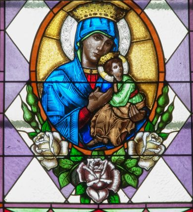 Zdjęcie nr 1: Witraż w kształcie stojącego prostokąta zamkniętego łukiem półkolistym ujęty geometryczną bordiurą wypełnioną motywem białych i niebieskich trójkątów oraz ciemnoczerwonych rombów. W polu ukośna kratka wypełniona ułożonymi naprzemiennie białymi i jasnofioletowymi rombami. W dolnej części witraża owalny medalion wsparty na girlandzie białych, kwitnących róż mieszczący popiersie Matki Boskiej z Dzieciątkiem ukazanej w typie Matki Boskiej Nieustającej Pomocy umieszczone na złotym tle. Maria zwrócona w trzech czwartych w lewo, na lewym przedramieniu trzyma siedzące Dzieciątko, prawą dłonią podtrzymuje dłonie Jezusa. Matka Boska ubrana jest w czerwoną suknię z długimi rękawami wykończoną przy dekolcie złotą lamówką oraz niebieski płaszcz zarzucony na głowę. Dzieciątko jest zwrócone w trzech czwartych w prawo z głową w przeciwnym kierunku. Jezus nosi jasnozieloną tunikę z długimi, szerokimi rękawami oraz złoty, szrafowany płaszcz, spod którego widoczne są bose stopy. Wokół głowy Marii znajduje się biały nimb wypełniony bordiurą roślinną, wokół głowy Dzieciątka nimb krzyżowy. Obie postaci ukazane są w złotych, kameryzowanych koronach typu otwartego. Powyżej medalionu prostokątne pole z napisem: „Fund[acja] Parafianki z Francji / Wykonano R[oku] P[ańskiego] 1939 za pobytu Ks[iędza] Prob[oszcza] Wł[adysława] Ziemińskiego”. 