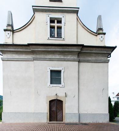 Zdjęcie nr 7: Kościół usytuowany jest w centrum miejscowości. Na plac kościelny prowadzi główne wejście od strony zachodniej oraz dwa mniejsze od strony północnej i południowej. Świątynia założona jest na planie krzyża łacińskiego, prezbiterium skierowane na zachód, równe szerokości nawy. Do korpusu kościoła przylega od strony zachodniej niższa i węższa zakrystia, a od strony południowej kruchta. Główne wejście do kościoła znajduje się od strony wschodniej przez czworoboczny przedsionek, nad którym wznosi się wieża. Portal z piaskowca, prosty o uszatych górnych narożach, w kluczu insygnia papieskie. W przedsionku od północnej strony zbudowane wewnętrzne, dwubiegowe schody kamienne prowadzące pierwotnie na chór muzyczny i wyższe piętra wieży. Na piętrze wejście do dwóch pomieszczeń usytuowanych na zapleczu chóru. Pomieszczenia te są nakryte stropami, oświetlone od południa i od wschodu. W pomieszczeniu południowym znajduje się kamienny próg z datą „1767”. Do przedsionka od strony południowej przylega kaplica Matki Boskiej Różańcowej założona na rzucie kwadratu, nakryta płaskim, malowanym stropem, wejście do kaplicy od strony północnej.

Wnętrze jest oświetlone przez 16 podłużnych okien, 8 w transepcie i 8 w ścianach nawy. Ponadto są jeszcze cztery okna okratowane, umieszczone jedno nad drugim po dwa w ścianie północnej i południowej.
Zakrystia jednoizbowa, dwa okna prostokątne w ścianie północno-zachodniej oraz dwoje drzwi, jedne do prezbiterium, drugie wejściowe w ścianie południowej. Wewnątrz zakrystii wąskie schody prowadzące do schowka na pięterku: jednoizbowego, oświetlonego od południa i od zachodu. Zakrystia i schowek nakryte płaskimi sufitami. Kruchta przybudowana do południowej ściany kościoła założona na rzucie kwadratu, o dwóch wejściach: z nawy i od zewnątrz od strony południowej. Wnętrze kościoła bez zaznaczonych podziałów architektonicznych, w dolnej części drewniana boazeria, w górnej iluzjonistyczna polichromia imitująca pilastry wspierające strop. Chór muzyczny wsparty na dwóch słupach.

Elewacja kościoła bez podziałów architektonicznych z zaznaczonym jedynie profilowanym gzymsem podokapowym. Fasada wschodnia trójosiowa ze środkowym ryzalitem, wieża włączona w korpus kościoła. W drugiej kondygnacji spływy flankujące wieżę, zakończone masywnymi sterczynami. Wieża nakryta dachem namiotowym z hełmem, na szczycie iglica. Na środku nawy ażurowa wieżyczka na sygnaturkę, nakryta daszkiem namiotowym z hełmem. Dach nad korpusem kościoła i zakrystią jednokalenicowy, dwuspadowy, nad prezbiterium i transeptem trójspadowy, nad kruchtą siodłowy.



