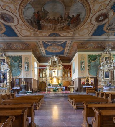 Zdjęcie nr 15: Kościół usytuowany jest w centrum miejscowości. Na plac kościelny prowadzi główne wejście od strony zachodniej oraz dwa mniejsze od strony północnej i południowej. Świątynia założona jest na planie krzyża łacińskiego, prezbiterium skierowane na zachód, równe szerokości nawy. Do korpusu kościoła przylega od strony zachodniej niższa i węższa zakrystia, a od strony południowej kruchta. Główne wejście do kościoła znajduje się od strony wschodniej przez czworoboczny przedsionek, nad którym wznosi się wieża. Portal z piaskowca, prosty o uszatych górnych narożach, w kluczu insygnia papieskie. W przedsionku od północnej strony zbudowane wewnętrzne, dwubiegowe schody kamienne prowadzące pierwotnie na chór muzyczny i wyższe piętra wieży. Na piętrze wejście do dwóch pomieszczeń usytuowanych na zapleczu chóru. Pomieszczenia te są nakryte stropami, oświetlone od południa i od wschodu. W pomieszczeniu południowym znajduje się kamienny próg z datą „1767”. Do przedsionka od strony południowej przylega kaplica Matki Boskiej Różańcowej założona na rzucie kwadratu, nakryta płaskim, malowanym stropem, wejście do kaplicy od strony północnej.

Wnętrze jest oświetlone przez 16 podłużnych okien, 8 w transepcie i 8 w ścianach nawy. Ponadto są jeszcze cztery okna okratowane, umieszczone jedno nad drugim po dwa w ścianie północnej i południowej.
Zakrystia jednoizbowa, dwa okna prostokątne w ścianie północno-zachodniej oraz dwoje drzwi, jedne do prezbiterium, drugie wejściowe w ścianie południowej. Wewnątrz zakrystii wąskie schody prowadzące do schowka na pięterku: jednoizbowego, oświetlonego od południa i od zachodu. Zakrystia i schowek nakryte płaskimi sufitami. Kruchta przybudowana do południowej ściany kościoła założona na rzucie kwadratu, o dwóch wejściach: z nawy i od zewnątrz od strony południowej. Wnętrze kościoła bez zaznaczonych podziałów architektonicznych, w dolnej części drewniana boazeria, w górnej iluzjonistyczna polichromia imitująca pilastry wspierające strop. Chór muzyczny wsparty na dwóch słupach.

Elewacja kościoła bez podziałów architektonicznych z zaznaczonym jedynie profilowanym gzymsem podokapowym. Fasada wschodnia trójosiowa ze środkowym ryzalitem, wieża włączona w korpus kościoła. W drugiej kondygnacji spływy flankujące wieżę, zakończone masywnymi sterczynami. Wieża nakryta dachem namiotowym z hełmem, na szczycie iglica. Na środku nawy ażurowa wieżyczka na sygnaturkę, nakryta daszkiem namiotowym z hełmem. Dach nad korpusem kościoła i zakrystią jednokalenicowy, dwuspadowy, nad prezbiterium i transeptem trójspadowy, nad kruchtą siodłowy.



