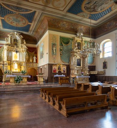 Zdjęcie nr 16: Kościół usytuowany jest w centrum miejscowości. Na plac kościelny prowadzi główne wejście od strony zachodniej oraz dwa mniejsze od strony północnej i południowej. Świątynia założona jest na planie krzyża łacińskiego, prezbiterium skierowane na zachód, równe szerokości nawy. Do korpusu kościoła przylega od strony zachodniej niższa i węższa zakrystia, a od strony południowej kruchta. Główne wejście do kościoła znajduje się od strony wschodniej przez czworoboczny przedsionek, nad którym wznosi się wieża. Portal z piaskowca, prosty o uszatych górnych narożach, w kluczu insygnia papieskie. W przedsionku od północnej strony zbudowane wewnętrzne, dwubiegowe schody kamienne prowadzące pierwotnie na chór muzyczny i wyższe piętra wieży. Na piętrze wejście do dwóch pomieszczeń usytuowanych na zapleczu chóru. Pomieszczenia te są nakryte stropami, oświetlone od południa i od wschodu. W pomieszczeniu południowym znajduje się kamienny próg z datą „1767”. Do przedsionka od strony południowej przylega kaplica Matki Boskiej Różańcowej założona na rzucie kwadratu, nakryta płaskim, malowanym stropem, wejście do kaplicy od strony północnej.

Wnętrze jest oświetlone przez 16 podłużnych okien, 8 w transepcie i 8 w ścianach nawy. Ponadto są jeszcze cztery okna okratowane, umieszczone jedno nad drugim po dwa w ścianie północnej i południowej.
Zakrystia jednoizbowa, dwa okna prostokątne w ścianie północno-zachodniej oraz dwoje drzwi, jedne do prezbiterium, drugie wejściowe w ścianie południowej. Wewnątrz zakrystii wąskie schody prowadzące do schowka na pięterku: jednoizbowego, oświetlonego od południa i od zachodu. Zakrystia i schowek nakryte płaskimi sufitami. Kruchta przybudowana do południowej ściany kościoła założona na rzucie kwadratu, o dwóch wejściach: z nawy i od zewnątrz od strony południowej. Wnętrze kościoła bez zaznaczonych podziałów architektonicznych, w dolnej części drewniana boazeria, w górnej iluzjonistyczna polichromia imitująca pilastry wspierające strop. Chór muzyczny wsparty na dwóch słupach.

Elewacja kościoła bez podziałów architektonicznych z zaznaczonym jedynie profilowanym gzymsem podokapowym. Fasada wschodnia trójosiowa ze środkowym ryzalitem, wieża włączona w korpus kościoła. W drugiej kondygnacji spływy flankujące wieżę, zakończone masywnymi sterczynami. Wieża nakryta dachem namiotowym z hełmem, na szczycie iglica. Na środku nawy ażurowa wieżyczka na sygnaturkę, nakryta daszkiem namiotowym z hełmem. Dach nad korpusem kościoła i zakrystią jednokalenicowy, dwuspadowy, nad prezbiterium i transeptem trójspadowy, nad kruchtą siodłowy.



