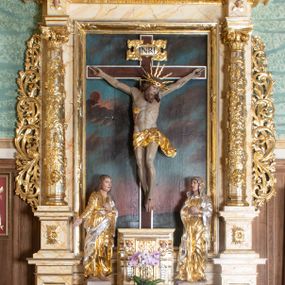 Zdjęcie nr 1: Nastawa ołtarzowa architektoniczna, dwukondygnacyjna, jednoosiowa z promienistą glorią w zwieńczeniu. Ołtarz prostopadłościenny, ustawiony na jednym stopniu, antependium zdobione dwiema prostokątnymi płycinami i środkową w kształcie kwadratu. Płyciny prostokątne wypełnione ornamentem akantowym, środkowa z medalionem, w polu którego umieszczony jest grecki krzyż o trójlistnie zakończonych ramionach, ukazany na tle czterech wiązek promieni. Tabernakulum w formie prostopadłościennej skrzynki z trzech stron flankowanej parami pilastrów hermowych, zamknięte profilowanym gzymsem. Drzwiczki w kształcie stojącego prostokąta, wypełnione rzeźbioną dekoracją manierystyczną. 

Dwukondygnacyjne retabulum ustawione jest na podwójnym cokole, ujęte parą pilastrów i ustawionych przed nimi kolumnami. Podpory wspierają wyłamane belkowanie i przerywany przyczółek, na którym usadzona jest para aniołków. Kolumny ustawione są na bazach, trzony bogato dekorowane winną latoroślą, ornamentem małżowinowo-chrząstkowym i główkami aniołków skierowanymi na wprost, kapitele kompozytowe. W polu głównym w prostokątnej, płytkiej wnęce umieszczony jest krucyfiks na tle malowanej Golgoty. Po bokach tabernakulum stoją ustawione rzeźby: św. Jana Ewangelisty po lewej stronie i Matki Boskiej po prawej stronie. Druga kondygnacja ustawiona na niskim cokole, ujęta parą zdwojonych pilastrów i parą kolumn podtrzymujących przerwane belkowanie, nad osią boczną ukośne, na którego szczycie usadzona jest para aniołków. W polu środkowym w ramie o kształcie stojącego prostokąta obraz św. Anny Samotrzeć. Na szczycie promienista gloria z półpostacią Boga Ojca na tle obłoków. Pierwsza i druga kondygnacja flankowane uszami z liści akantu. W partii fryzu dwie niewielkie główki aniołków, w pierwszej strefie cokołowej płyciny z liśćmi akantu, a w drugiej rozety. Struktura marmoryzowana w kolorze jasnobeżowym z czerwonym, brązowym i żółtym żyłkowaniem; ornamentyka i detale złocone oraz srebrzone.