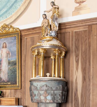 Zdjęcie nr 1: Chrzcielnica ustawiona na dwóch stopniach na rzucie półkolistym, wsparta na ośmiobocznej stopie z napisem „HOC BAPTISTERIUM EST CONSTRUCTUM MDCXXXVIII ”. Trzon ośmioboczny z ośmiobocznym pierścieniem pośrodku, ozdobionym rozetkami. Czara wysoka, ośmioboczna, zdobiona od dołu rzeźbionym ząbkowym pasem dekoracyjnym, powyżej stylizowanymi liliami andegaweńskimi, a od góry pasem liści. Pokrywa w formie małej aediculi, wsparta na sześciu kolumnach, które unoszą półkolistą kopułę. Podpory o gładkich i złoconych trzonach, kapitele jońskie. Zwieńczenie o profilowanym gzymsie, kopuła zdobiona girlandami, a na szczycie kimationem. Na kopule ustawiona grupa rzeźbiarska przedstawiająca św. Jana Chrzciciela i Chrystusa. Polichromia w odsłoniętych partiach ciała naturalistyczna, detale i ornamentyka złocone i srebrzone, kopuła polichromowana na kolor jasnobeżowy.

