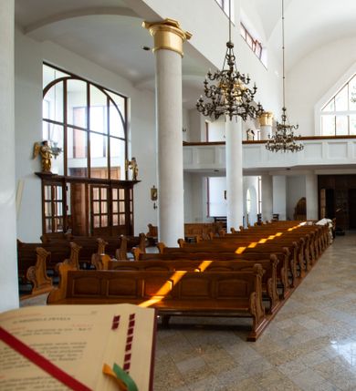 Zdjęcie nr 5: Kościół murowany, tynkowany, trójnawowy, bazylikowy. Prezbiterium prostokątne, zamknięte prosto, do północnej ściany przylega zakrystia. Nawa główna na planie prostokąta, o szerokości prezbiterium, nawy boczne węższe i krótsze. Na ich zakończeniu dostawione dwie wieże na planie kwadratu. Do południowej ściany korpusu nawowego przylega prostokątna kaplica, ustawiona pod kątem, otwarta do nawy prostokątnym prześwitem, z drzwiami w dolnej połowie i oknem w górnej. Prezbiterium i nawa główna sklepione kolebkowo z lunetami, nawy boczne kolebkowo. Nawa główna oddzielona od bocznych czterema parami kolumn. Parapet chóru muzycznego w zachodniej części nawy. Posadzka z płyt ceramicznych. 
Fasada zakończona trójkątnym szczytem. Na osi portal w formie stojącego prostokąta zamkniętego trójkątnie, w opasce tynkowej. W dolnej połowie dwuskrzydłowe drzwi, górna połowa przeszklona, podzielona na kwatery. Wieże pięciokondygnacyjne. Z wąskimi, przeszklonymi prześwitami przez cztery pierwsze kondygnacje na dwóch bokach. W piątej po dwa otwory dzwonne w formie stojącego prostokąta na każdej z czterech ścian. Wieże zwieńczone daszkami czterospadowymi oraz latarniami z otworami dzwonnymi, zakończonymi dachami wieżowymi z krzyżami. Pomiędzy fasadą a wieżami wąskie partie muru z przeszklonymi prześwitami. Na elewacjach bocznych nawy głównej, ponad dachami naw bocznych po trzy okna w formie wydłużonego leżącego prostokąta. Na elewacji północnej duże okno w formie leżącego prostokąta zamkniętego łukiem półkolistym. Kaplica południowa z wejściem na ścianie zachodniej, w formie drewnianego portalu w kształcie stojącego prostokąta, z dwuskrzydłowymi drzwiami, z kwadratowym oknem ponad. Na jej ścianie południowej dwa duże okna w kształcie leżącego prostokąta, na dwóch poziomach. Elewacja wschodnia zakończona trójkątnym szczytem. 
Nawa główna i prezbiterium nakryte dachami dwuspadowymi, nawy boczne pulpitowymi, kaplica dwuspadowym. Pomiędzy nawą a prezbiterium wieżyczka na sygnaturkę z latarnią, nakryta dachem wieżowym.  





