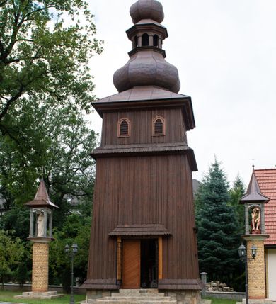 Zdjęcie nr 1: Dzwonnica drewniana, konstrukcji słupowo-ramowej, ściany szalowane z listwowaniem, więźba dachowa drewniana. Założona na planie kwadratu, na kamiennym podmurowaniu, przesłoniętym okapowym daszkiem gontowym. Ściany zwężające się ku górze, przepasane okapowym daszkiem gontowym w trzech czwartych wysokości. Zwieńczona blaszanym hełmem baniastym zakończonym szpikulcem z kulą i krzyżem. Otwór drzwiowy w ścianie południowej o wykroju stojącego prostokąta zamknięty drzwiami dwuskrzydłowymi, nakryty okapowym daszkiem gontowym. Do drzwi prowadzą czterostopniowe, kamienne schody. Otwory głosowe w formie stojącego prostokąta zamkniętego łukiem półkolistym nadwieszonym, po dwa na każdej ścianie w najwyższej partii dzwonnicy.