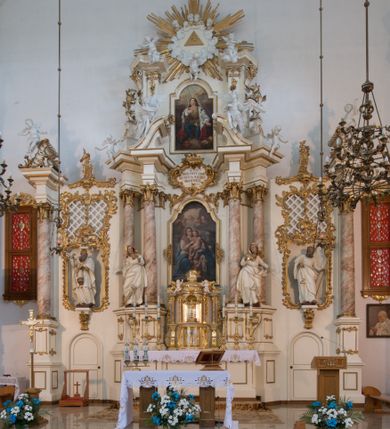 Zdjęcie nr 46: Nastawa architektoniczna, trójosiowa, dwukondygnacyjna ze zwieńczeniem, ustawiona na dwustrefowym cokole. Ołtarz drewniany, prostopadłościenny z drewnianą mensą, w partii antepedium dekorowany trzema płycinami. Na ołtarzu ustawione tabernakulum. Cokół dwustrefowy z wyodrębnionymi prostopadłościanami dekorowanymi w pierwszej strefie płycinami, w drugiej rocaille'owymi płycinami.  Osie pierwszej kondygnacji wydzielone trzema parami kolumn. Oś środkowa flankowana dwiema parami pilastrów i stojącymi przed nimi kolumnami ustawionymi na cokołach, druga para zwrócona pod kątem na zewnątrz. Podpory dźwigają wyłamane na ich osi fragmenty belkowania, środkowa para również przerwany, falisty przyczółek. Na belkowaniu i przyczółku siedzi para puttów i para adorujących aniołów. Pomiędzy parami kolumn ustawione figury św. Anny i św. Elżbiety. W polu głównym znajduje się wnęka w formie stojącego prostokąta zamkniętego łukiem półkolistym nadwieszonym z uskokiem, ujęta profilowaną ramą z obrazem Matki Boskiej z Dzieciątkiem i św. Janem Chrzcicielem. Ponad obrazem rokokowy kartusz z kwiatowymi zwisami, z napisem „EN! / PORTA PATET CURIAE / DEI EXCELSA MATER ET / VIRGO IO! VENITE / S(anctus) Cyprianus”. Osie boczne wydzielone zewnętrzną parą pilastrów i stojących przed nimi kolumn ustawionych na dwustrefowych cokołach, dźwigających imposty i fragmenty przerwanego rocaille'owego przyczółka. Na osiach w partii cokołu znajdują się bramki z drzwiami w kształcie stojącego prostokąta zamkniętego łukiem półkolistym. Ponad nimi na rocaille'owych konsolach, na tle wnęki ujętej rocaille'ową ramą znajdują się figury św. Joachima i Zachariasza. Nad wnękami ażurowa kratka w formie stojącego prostokąta ujęta rocaille'ową ramą. Całość zamknięta rocaille'm z wyodrębnionym pionowym akcentem koguciego grzebienia. Druga kondygnacja flankowana dwiema parami pilastrów, w tym zewnętrzną ustawioną pod kątem na zewnątrz o trzonach przechodzących w spływy wolutowe ustawione na cokołach na belkowaniu pierwszej kondygnacji nastawy. Spływy zakończone są rokokowymi wazonami. Podpory dźwigają gzyms przerwany na polem. Całość zamknięta medalionem z Okiem Opatrzności otoczonym wieńcem z obłoków i uskrzydlonych główek anielskich, w glorii promienistej. U dołu medalionu i na gzymsie znajdują się putta. W polu wnęka w formie stojącego prostokąta zamkniętego łukiem półkolistym nadwieszonym w profilowanej ramie z obrazem św. Kazimierza. Struktura niemal w całości polichromowana w kolorze białym, trzony kolumn polichromowane na sposób imitujący marmoryzację w kolorze biało-różowym, profile i ornamentyka złocone. 