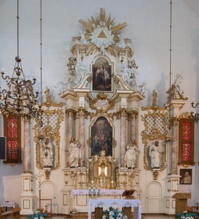 Zdjęcie nr 1: Nastawa architektoniczna, trójosiowa, dwukondygnacyjna ze zwieńczeniem, ustawiona na dwustrefowym cokole. Ołtarz drewniany, prostopadłościenny z drewnianą mensą, w partii antepedium dekorowany trzema płycinami. Na ołtarzu ustawione tabernakulum. Cokół dwustrefowy z wyodrębnionymi prostopadłościanami dekorowanymi w pierwszej strefie płycinami, w drugiej rocaille'owymi płycinami.  Osie pierwszej kondygnacji wydzielone trzema parami kolumn. Oś środkowa flankowana dwiema parami pilastrów i stojącymi przed nimi kolumnami ustawionymi na cokołach, druga para zwrócona pod kątem na zewnątrz. Podpory dźwigają wyłamane na ich osi fragmenty belkowania, środkowa para również przerwany, falisty przyczółek. Na belkowaniu i przyczółku siedzi para puttów i para adorujących aniołów. Pomiędzy parami kolumn ustawione figury św. Anny i św. Elżbiety. W polu głównym znajduje się wnęka w formie stojącego prostokąta zamkniętego łukiem półkolistym nadwieszonym z uskokiem, ujęta profilowaną ramą z obrazem Matki Boskiej z Dzieciątkiem i św. Janem Chrzcicielem. Ponad obrazem rokokowy kartusz z kwiatowymi zwisami, z napisem „EN! / PORTA PATET CURIAE / DEI EXCELSA MATER ET / VIRGO IO! VENITE / S(anctus) Cyprianus”. Osie boczne wydzielone zewnętrzną parą pilastrów i stojących przed nimi kolumn ustawionych na dwustrefowych cokołach, dźwigających imposty i fragmenty przerwanego rocaille'owego przyczółka. Na osiach w partii cokołu znajdują się bramki z drzwiami w kształcie stojącego prostokąta zamkniętego łukiem półkolistym. Ponad nimi na rocaille'owych konsolach, na tle wnęki ujętej rocaille'ową ramą znajdują się figury św. Joachima i Zachariasza. Nad wnękami ażurowa kratka w formie stojącego prostokąta ujęta rocaille'ową ramą. Całość zamknięta rocaille'm z wyodrębnionym pionowym akcentem koguciego grzebienia. Druga kondygnacja flankowana dwiema parami pilastrów, w tym zewnętrzną ustawioną pod kątem na zewnątrz o trzonach przechodzących w spływy wolutowe ustawione na cokołach na belkowaniu pierwszej kondygnacji nastawy. Spływy zakończone są rokokowymi wazonami. Podpory dźwigają gzyms przerwany na polem. Całość zamknięta medalionem z Okiem Opatrzności otoczonym wieńcem z obłoków i uskrzydlonych główek anielskich, w glorii promienistej. U dołu medalionu i na gzymsie znajdują się putta. W polu wnęka w formie stojącego prostokąta zamkniętego łukiem półkolistym nadwieszonym w profilowanej ramie z obrazem św. Kazimierza. Struktura niemal w całości polichromowana w kolorze białym, trzony kolumn polichromowane na sposób imitujący marmoryzację w kolorze biało-różowym, profile i ornamentyka złocone. 