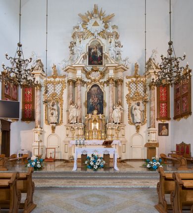 Zdjęcie nr 45: Nastawa architektoniczna, trójosiowa, dwukondygnacyjna ze zwieńczeniem, ustawiona na dwustrefowym cokole. Ołtarz drewniany, prostopadłościenny z drewnianą mensą, w partii antepedium dekorowany trzema płycinami. Na ołtarzu ustawione tabernakulum. Cokół dwustrefowy z wyodrębnionymi prostopadłościanami dekorowanymi w pierwszej strefie płycinami, w drugiej rocaille'owymi płycinami.  Osie pierwszej kondygnacji wydzielone trzema parami kolumn. Oś środkowa flankowana dwiema parami pilastrów i stojącymi przed nimi kolumnami ustawionymi na cokołach, druga para zwrócona pod kątem na zewnątrz. Podpory dźwigają wyłamane na ich osi fragmenty belkowania, środkowa para również przerwany, falisty przyczółek. Na belkowaniu i przyczółku siedzi para puttów i para adorujących aniołów. Pomiędzy parami kolumn ustawione figury św. Anny i św. Elżbiety. W polu głównym znajduje się wnęka w formie stojącego prostokąta zamkniętego łukiem półkolistym nadwieszonym z uskokiem, ujęta profilowaną ramą z obrazem Matki Boskiej z Dzieciątkiem i św. Janem Chrzcicielem. Ponad obrazem rokokowy kartusz z kwiatowymi zwisami, z napisem „EN! / PORTA PATET CURIAE / DEI EXCELSA MATER ET / VIRGO IO! VENITE / S(anctus) Cyprianus”. Osie boczne wydzielone zewnętrzną parą pilastrów i stojących przed nimi kolumn ustawionych na dwustrefowych cokołach, dźwigających imposty i fragmenty przerwanego rocaille'owego przyczółka. Na osiach w partii cokołu znajdują się bramki z drzwiami w kształcie stojącego prostokąta zamkniętego łukiem półkolistym. Ponad nimi na rocaille'owych konsolach, na tle wnęki ujętej rocaille'ową ramą znajdują się figury św. Joachima i Zachariasza. Nad wnękami ażurowa kratka w formie stojącego prostokąta ujęta rocaille'ową ramą. Całość zamknięta rocaille'm z wyodrębnionym pionowym akcentem koguciego grzebienia. Druga kondygnacja flankowana dwiema parami pilastrów, w tym zewnętrzną ustawioną pod kątem na zewnątrz o trzonach przechodzących w spływy wolutowe ustawione na cokołach na belkowaniu pierwszej kondygnacji nastawy. Spływy zakończone są rokokowymi wazonami. Podpory dźwigają gzyms przerwany na polem. Całość zamknięta medalionem z Okiem Opatrzności otoczonym wieńcem z obłoków i uskrzydlonych główek anielskich, w glorii promienistej. U dołu medalionu i na gzymsie znajdują się putta. W polu wnęka w formie stojącego prostokąta zamkniętego łukiem półkolistym nadwieszonym w profilowanej ramie z obrazem św. Kazimierza. Struktura niemal w całości polichromowana w kolorze białym, trzony kolumn polichromowane na sposób imitujący marmoryzację w kolorze biało-różowym, profile i ornamentyka złocone. 