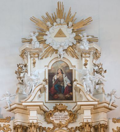 Zdjęcie nr 58: Nastawa architektoniczna, trójosiowa, dwukondygnacyjna ze zwieńczeniem, ustawiona na dwustrefowym cokole. Ołtarz drewniany, prostopadłościenny z drewnianą mensą, w partii antepedium dekorowany trzema płycinami. Na ołtarzu ustawione tabernakulum. Cokół dwustrefowy z wyodrębnionymi prostopadłościanami dekorowanymi w pierwszej strefie płycinami, w drugiej rocaille'owymi płycinami.  Osie pierwszej kondygnacji wydzielone trzema parami kolumn. Oś środkowa flankowana dwiema parami pilastrów i stojącymi przed nimi kolumnami ustawionymi na cokołach, druga para zwrócona pod kątem na zewnątrz. Podpory dźwigają wyłamane na ich osi fragmenty belkowania, środkowa para również przerwany, falisty przyczółek. Na belkowaniu i przyczółku siedzi para puttów i para adorujących aniołów. Pomiędzy parami kolumn ustawione figury św. Anny i św. Elżbiety. W polu głównym znajduje się wnęka w formie stojącego prostokąta zamkniętego łukiem półkolistym nadwieszonym z uskokiem, ujęta profilowaną ramą z obrazem Matki Boskiej z Dzieciątkiem i św. Janem Chrzcicielem. Ponad obrazem rokokowy kartusz z kwiatowymi zwisami, z napisem „EN! / PORTA PATET CURIAE / DEI EXCELSA MATER ET / VIRGO IO! VENITE / S(anctus) Cyprianus”. Osie boczne wydzielone zewnętrzną parą pilastrów i stojących przed nimi kolumn ustawionych na dwustrefowych cokołach, dźwigających imposty i fragmenty przerwanego rocaille'owego przyczółka. Na osiach w partii cokołu znajdują się bramki z drzwiami w kształcie stojącego prostokąta zamkniętego łukiem półkolistym. Ponad nimi na rocaille'owych konsolach, na tle wnęki ujętej rocaille'ową ramą znajdują się figury św. Joachima i Zachariasza. Nad wnękami ażurowa kratka w formie stojącego prostokąta ujęta rocaille'ową ramą. Całość zamknięta rocaille'm z wyodrębnionym pionowym akcentem koguciego grzebienia. Druga kondygnacja flankowana dwiema parami pilastrów, w tym zewnętrzną ustawioną pod kątem na zewnątrz o trzonach przechodzących w spływy wolutowe ustawione na cokołach na belkowaniu pierwszej kondygnacji nastawy. Spływy zakończone są rokokowymi wazonami. Podpory dźwigają gzyms przerwany na polem. Całość zamknięta medalionem z Okiem Opatrzności otoczonym wieńcem z obłoków i uskrzydlonych główek anielskich, w glorii promienistej. U dołu medalionu i na gzymsie znajdują się putta. W polu wnęka w formie stojącego prostokąta zamkniętego łukiem półkolistym nadwieszonym w profilowanej ramie z obrazem św. Kazimierza. Struktura niemal w całości polichromowana w kolorze białym, trzony kolumn polichromowane na sposób imitujący marmoryzację w kolorze biało-różowym, profile i ornamentyka złocone. 