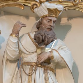 Zdjęcie nr 1: Rzeźba drążona z tyłu, ustawiona na niskiej podstawie. Postać zwrócona frontalnie, z opuszczona głową skierowaną w lewo. W lewej, ugiętej i uniesionej z przodu ręce trzyma złoconą kadzielnicę na łańcuszkach, które podtrzymuje również w uniesionej prawej ręce. Twarz ma pociągłą, o starczych rysach, dużych, migdałowatych i blisko siebie osadzonych oczach, dużym, prostym nosie i rozchylonych ustach, okoloną gęstą, silnie skręconą i uniesioną brodą oraz krótkimi włosami. Na głowie ma nakrycie kapłana. Ubrany jest w długą, białą suknię spodnią ze złoconymi lamówkami oraz białą suknię wierzchnią, sięgającą kolan, dekorowaną przy dolnej krawędzi złoconymi chwostami, przepasaną w talii złoconym pasem. Na ramiona ma narzucony biały płaszcz ze złoconymi lamówkami, opadający po bokach postaci, zaś na piersi ma złocony pektorał. Partie ciała polichromowane naturalistycznie.