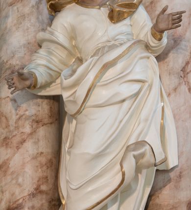 Zdjęcie nr 5: Rzeźba drążona z tyłu, ustawiona na niewielkiej podstawie. Święta zwrócona w trzech czwartych w lewo, w kontrapoście, z rękami rozłożonymi na boki. Twarz ma szczupłą, o starczych rysach, wyraźnie podkreślonej linii żuchwy, małych, migdałowatych oczach, prostym nosie i małych, rozchylonych ustach, okoloną włosami schowanymi pod welonem. Ubrana jest w długą, białą tunikę ze złoconą lamówką oraz biały płaszcz ze złoconą lamówką, zawinięty wokół prawego ramienia oraz wokół bioder, na głowie ma złocony welon z rozwianymi fragmentami tkaniny. Ciało polichromowane naturalistycznie. 