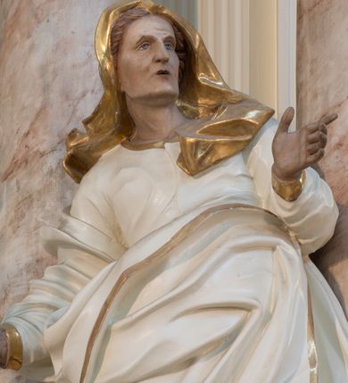 Zdjęcie nr 7: Rzeźba drążona z tyłu, ustawiona na niewielkiej podstawie. Święta zwrócona w trzech czwartych w lewo, w kontrapoście, z rękami rozłożonymi na boki. Twarz ma szczupłą, o starczych rysach, wyraźnie podkreślonej linii żuchwy, małych, migdałowatych oczach, prostym nosie i małych, rozchylonych ustach, okoloną włosami schowanymi pod welonem. Ubrana jest w długą, białą tunikę ze złoconą lamówką oraz biały płaszcz ze złoconą lamówką, zawinięty wokół prawego ramienia oraz wokół bioder, na głowie ma złocony welon z rozwianymi fragmentami tkaniny. Ciało polichromowane naturalistycznie. 